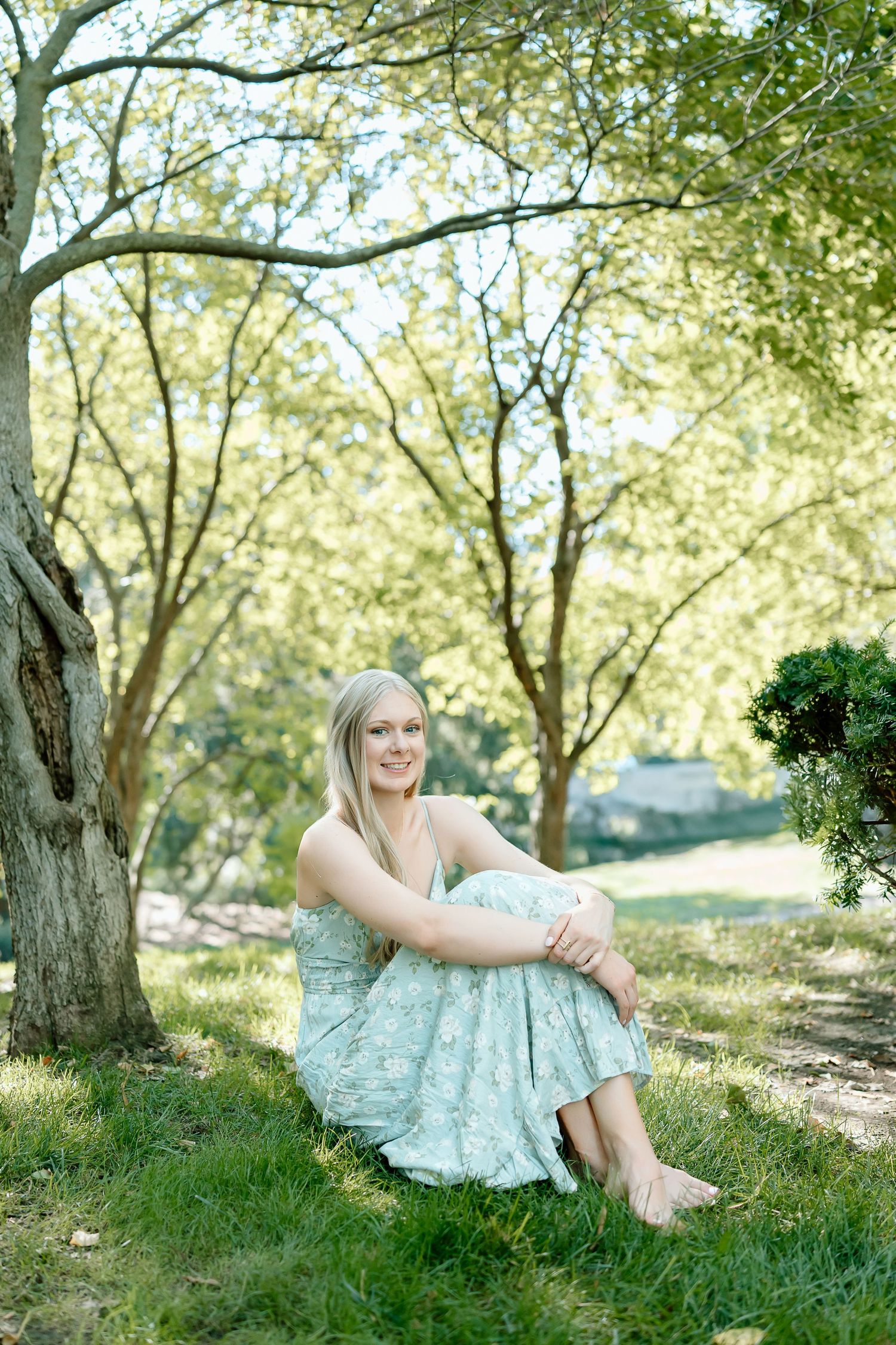 A person in a light blue dress relaxes on grassy ground under blooming spring trees in natural sunlight.