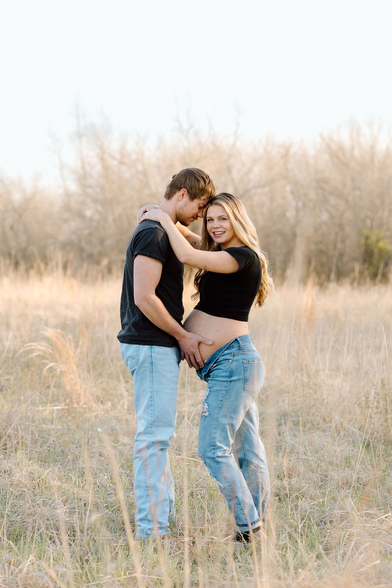 Romantic couple embracing in tall autumn grass during golden hour sunset in a rustic field setting.