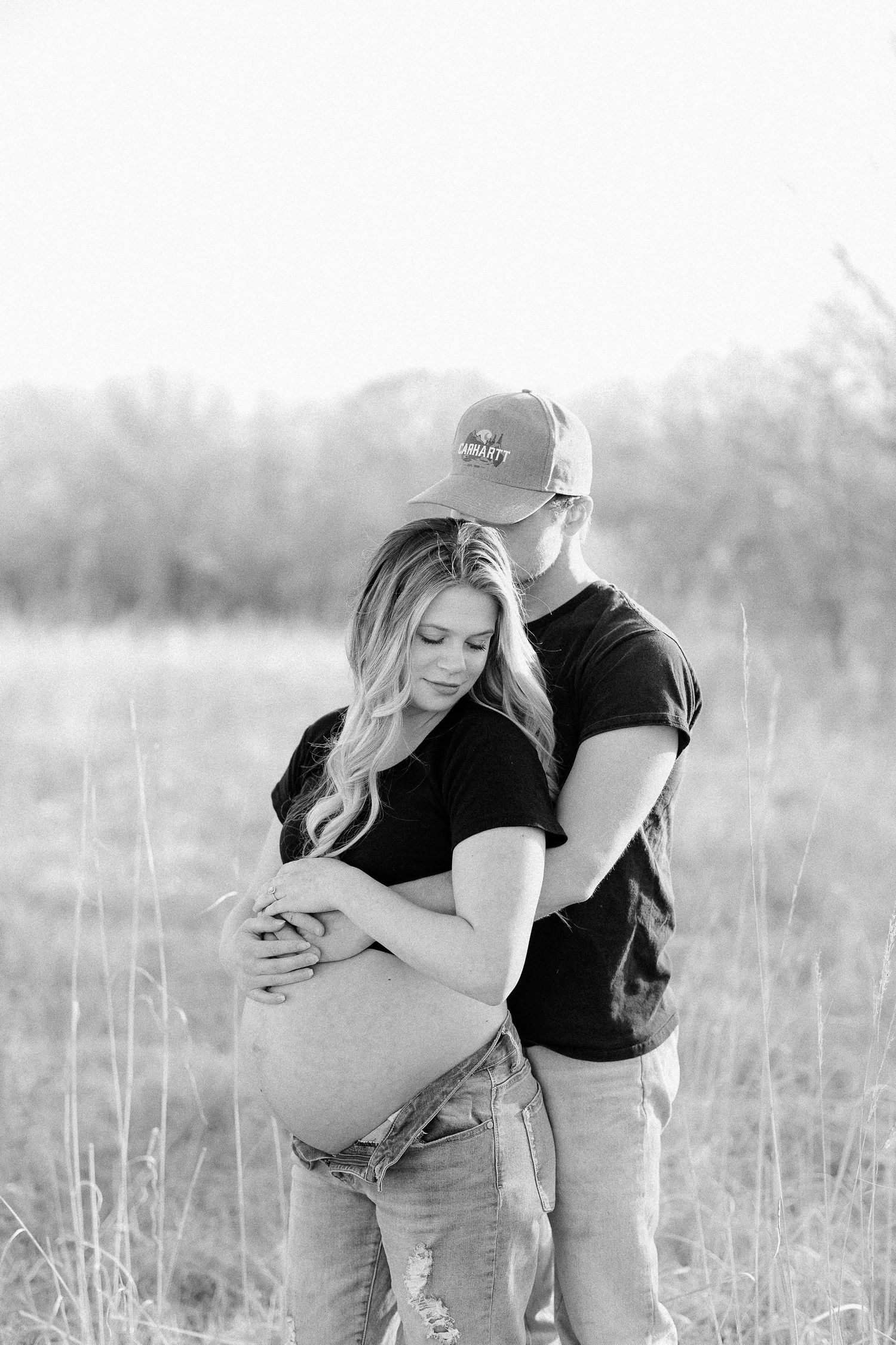 A romantic black and white photo series showing a couple embracing in a serene field of tall grass.
