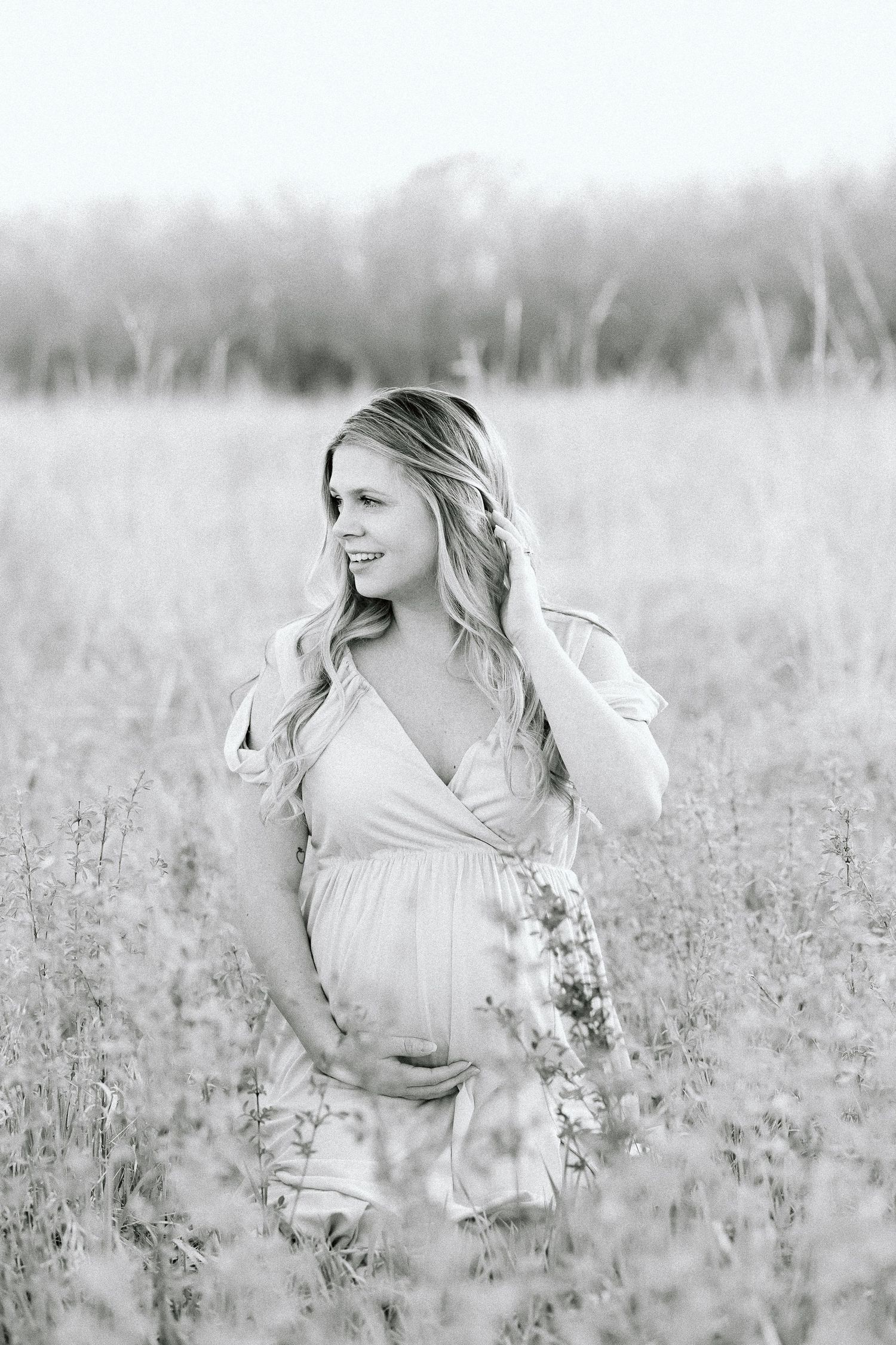 Black and white maternity photo of an expectant mother in a flowy dress standing in a wildflower field.