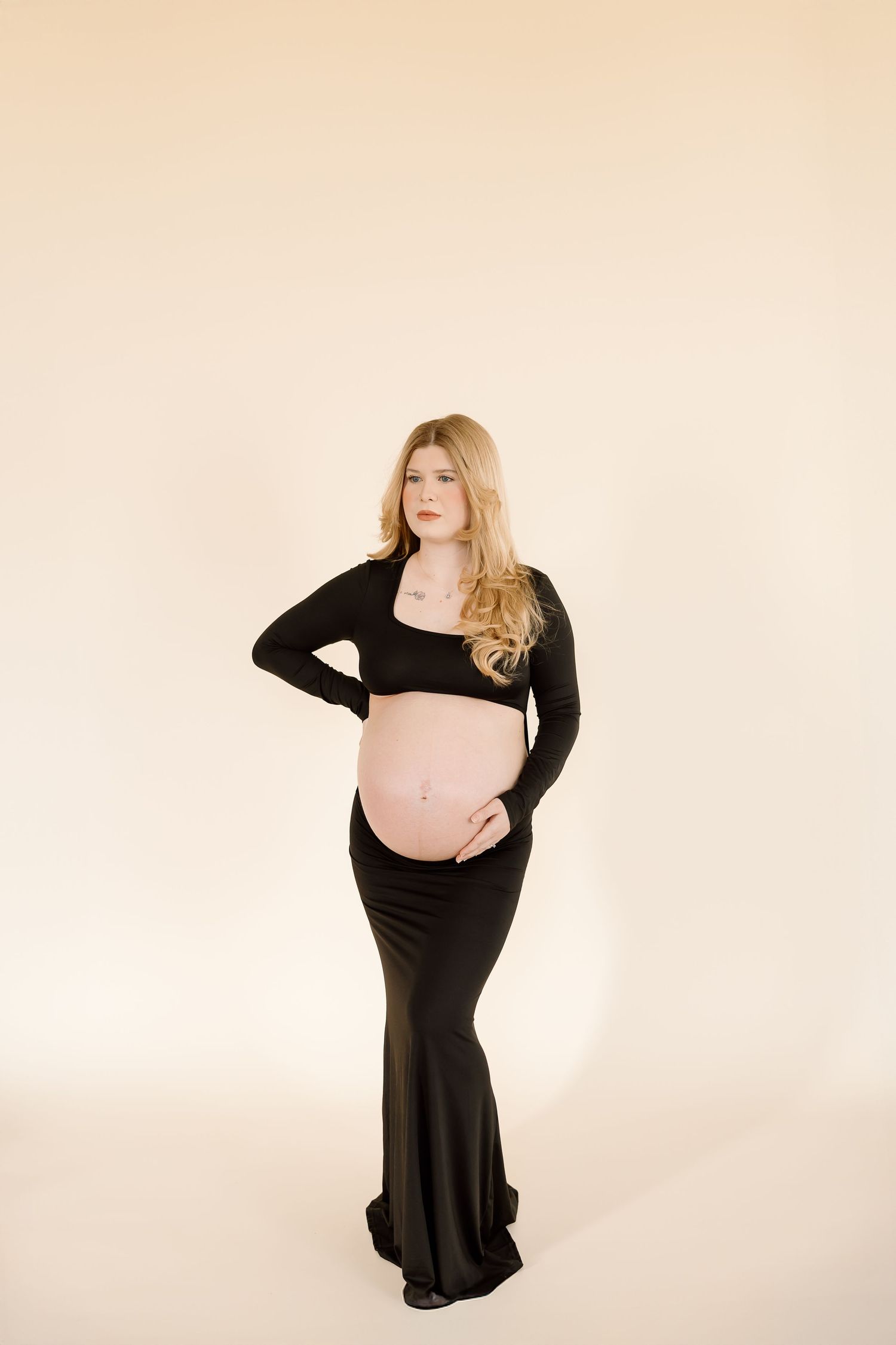 A pregnant woman in a black dress poses against a white backdrop in a series of artistic maternity photos.