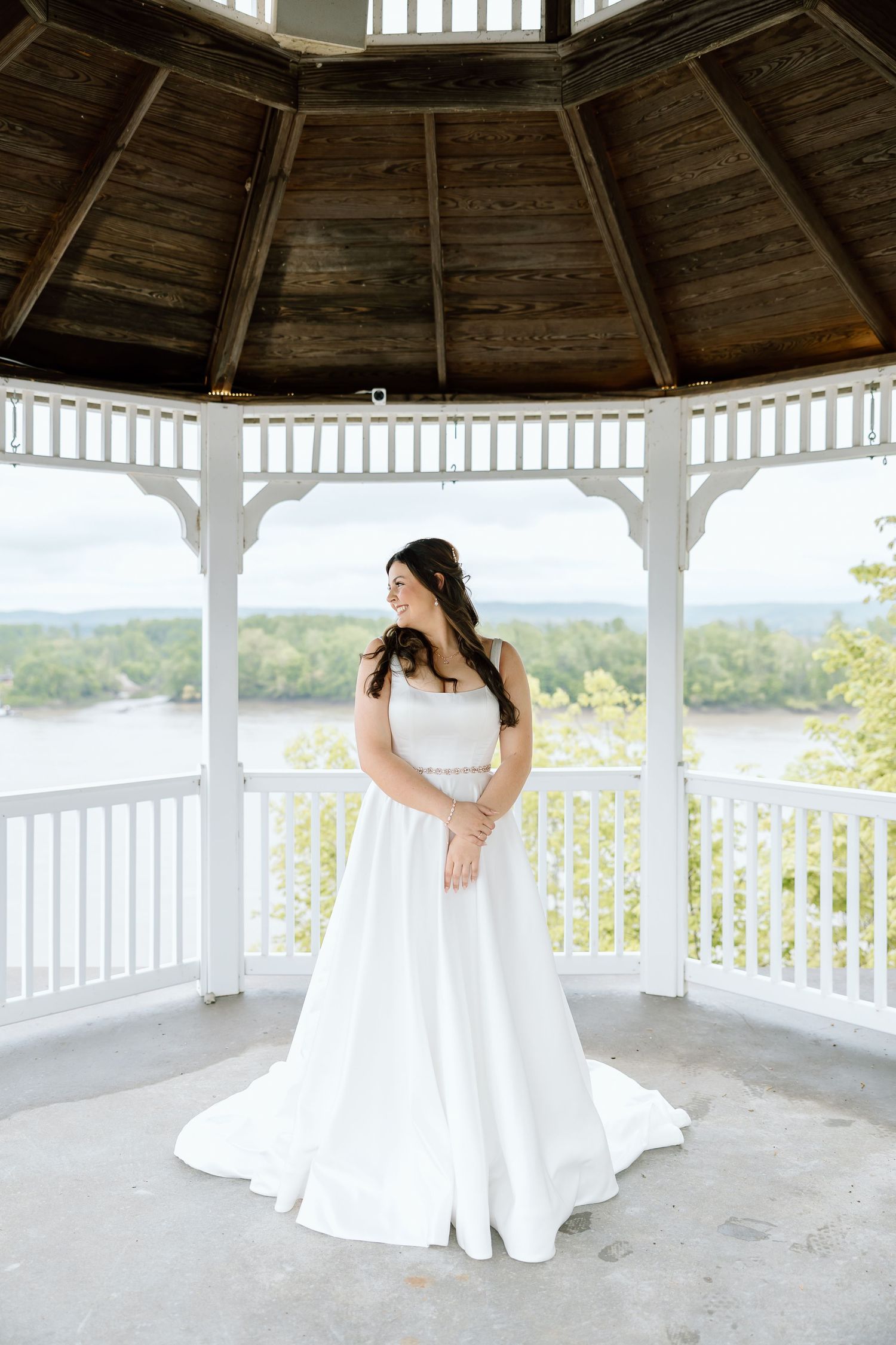 A white wedding dress flows gracefully in a rustic wooden gazebo overlooking a scenic mountain landscape.