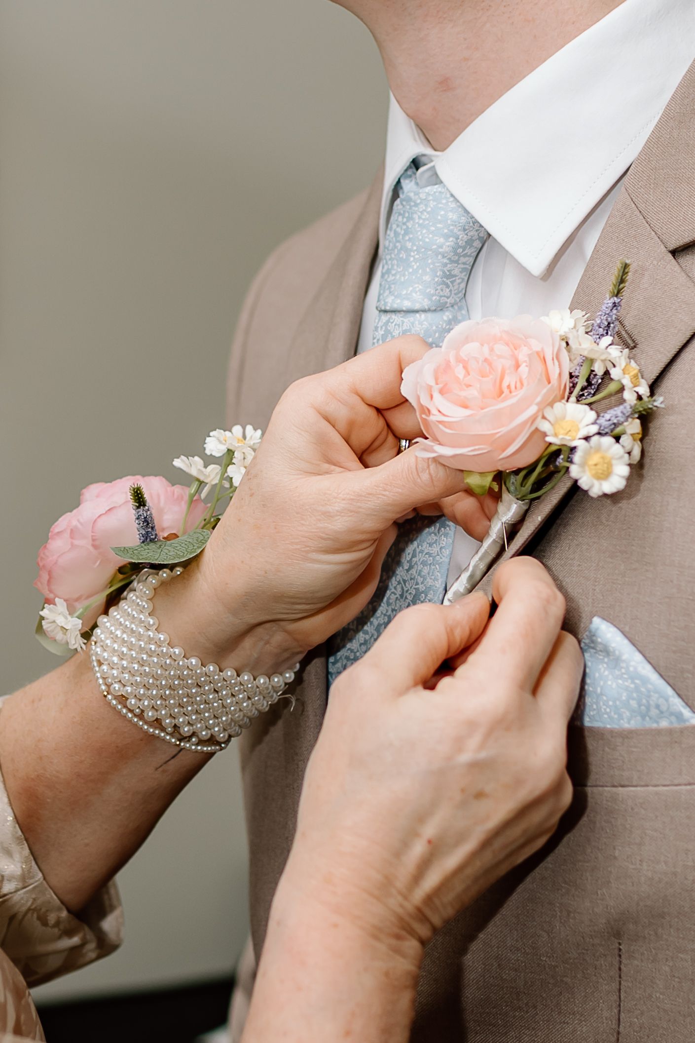 A series of hands pinning a peach-colored rose boutonniere to a tan suit lapel for a formal occasion.