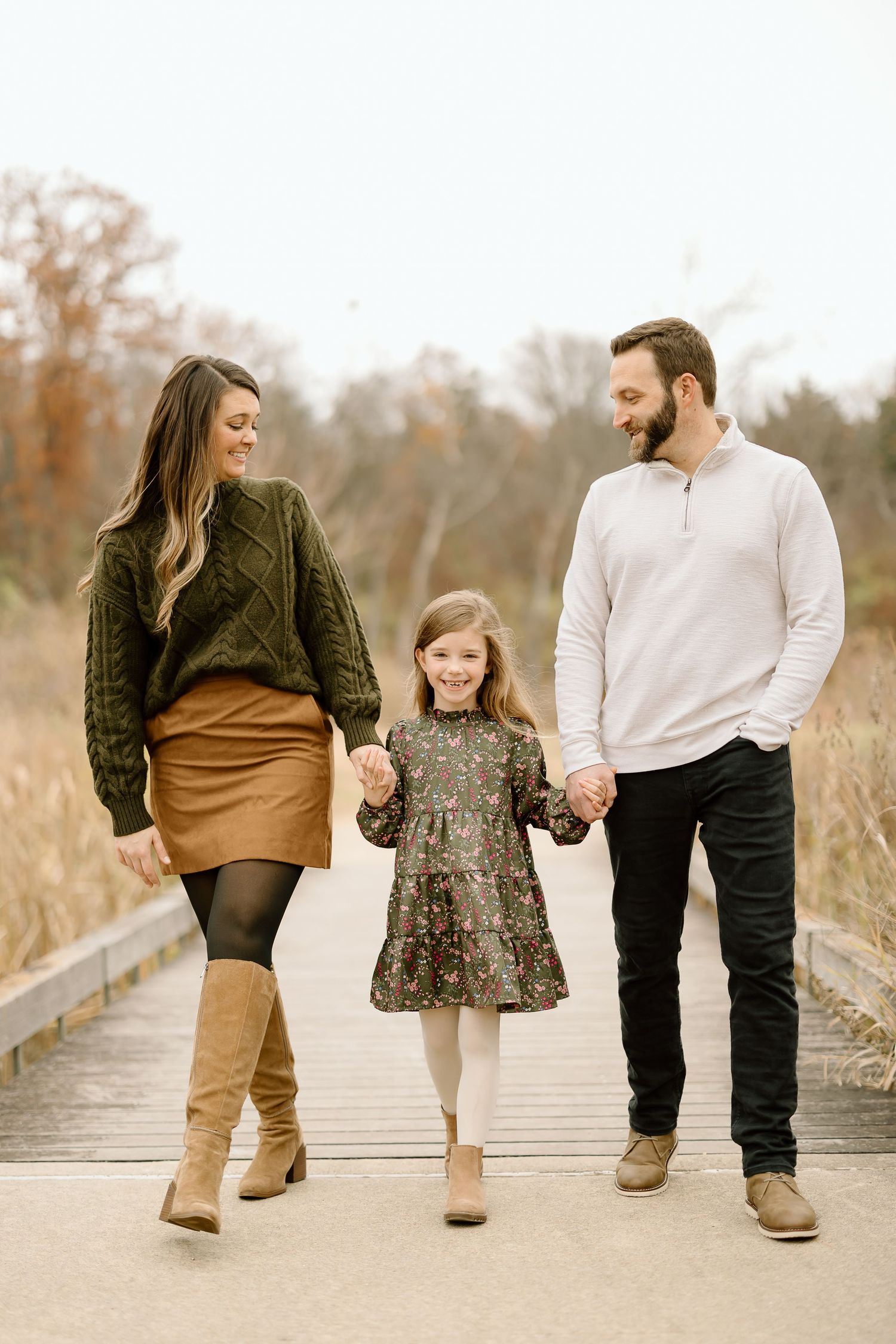 Family walking hand in hand on wooden boardwalk during fall season.