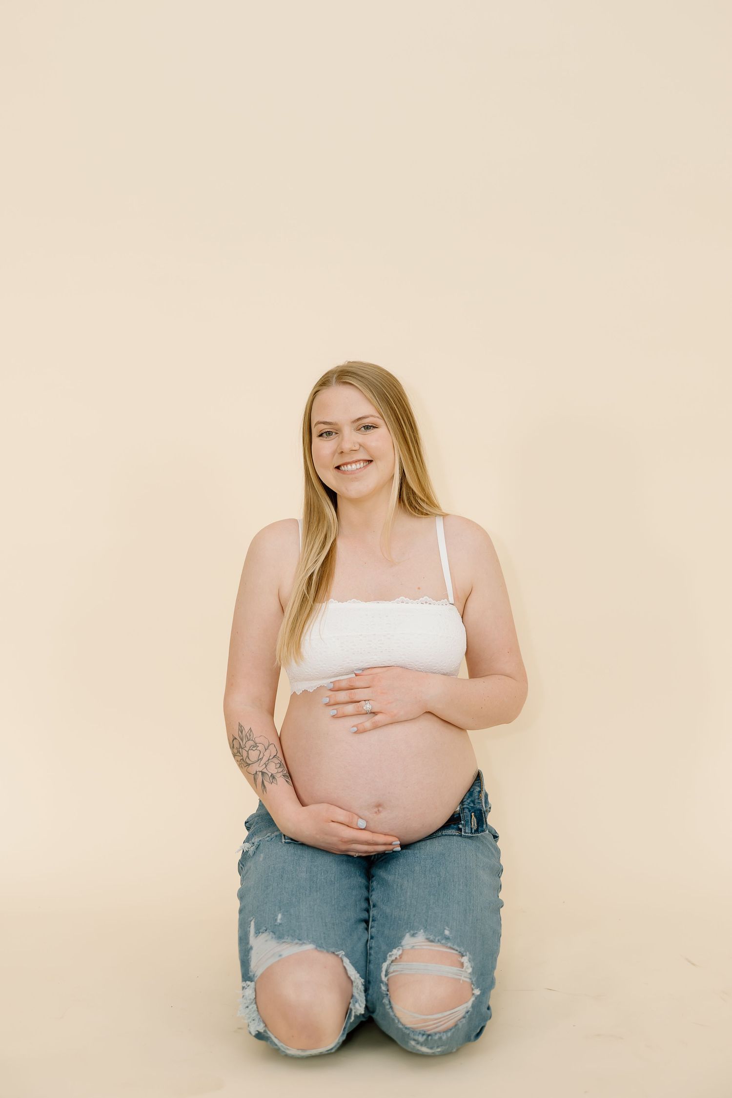 A radiant mother-to-be poses on her knees in casual attire for a maternity portrait.