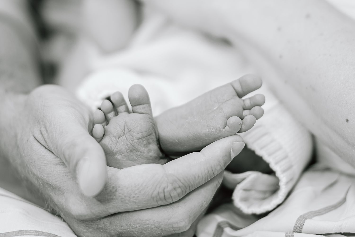 Close-up black and white shot of tiny newborn baby feet held in adult hands.