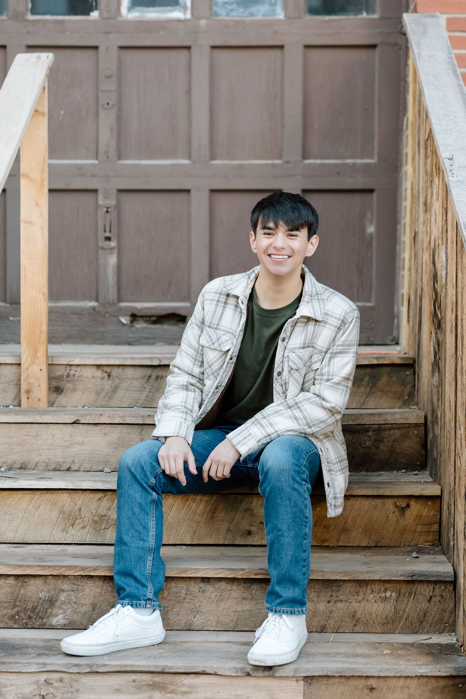 Person in plaid jacket sitting on wooden steps with warm expression.