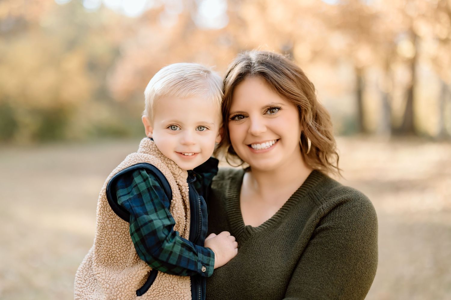 A close-up portrait shows a parent and child smiling together during a fall photoshoot.