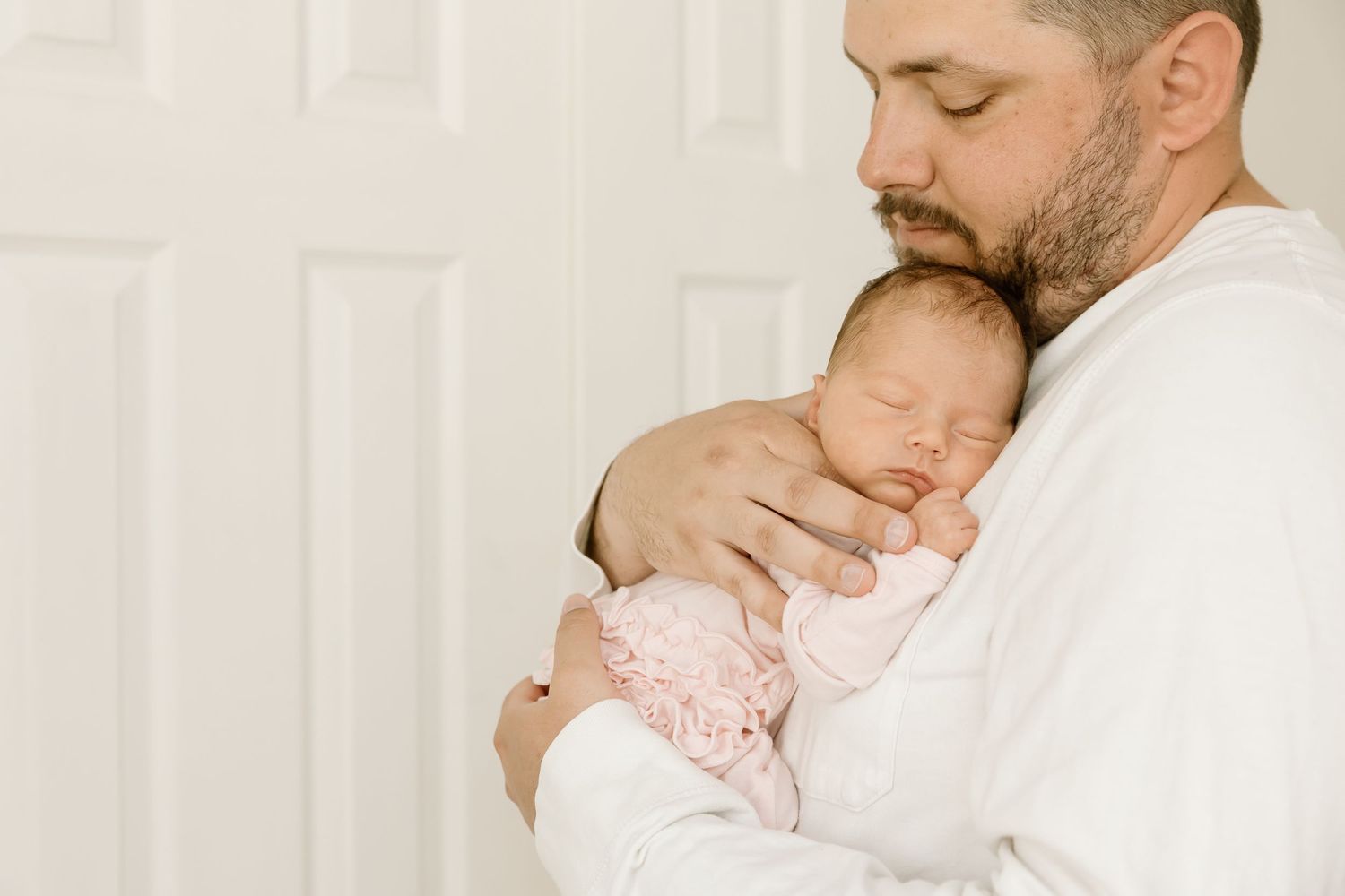 Tender moment showing sleeping infant being held against white shirt.