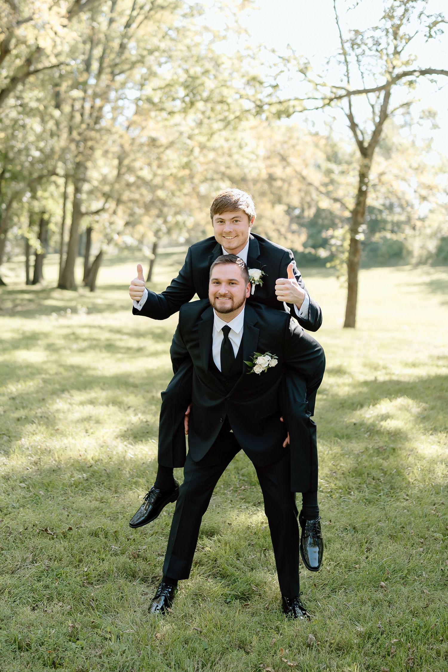 A playful sequence of groomsmen posing and running across a grassy lawn in formal black suits.