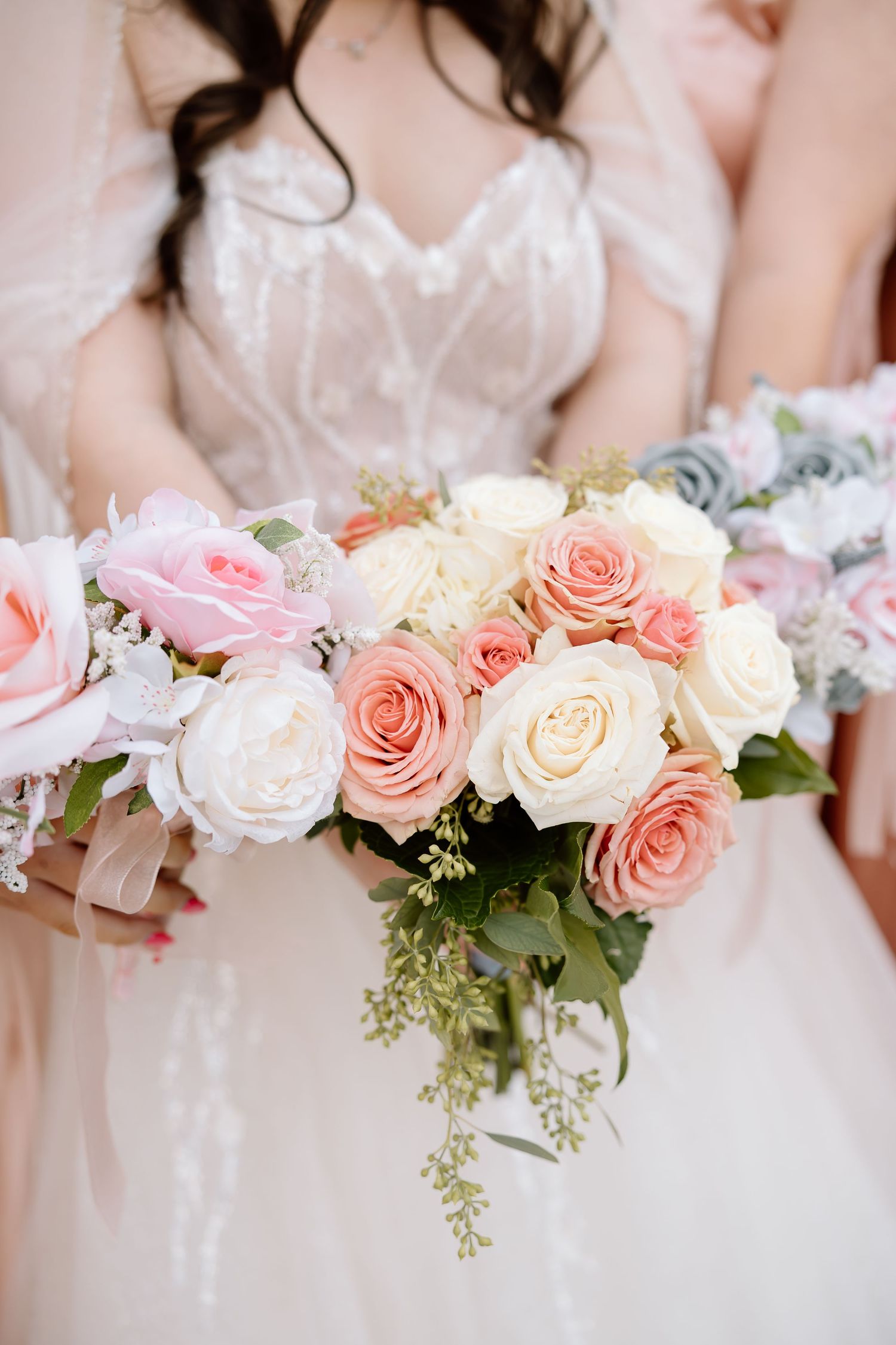 A row of wedding bouquets featuring pink and white roses with eucalyptus greenery held by bridesmaids in soft focus.