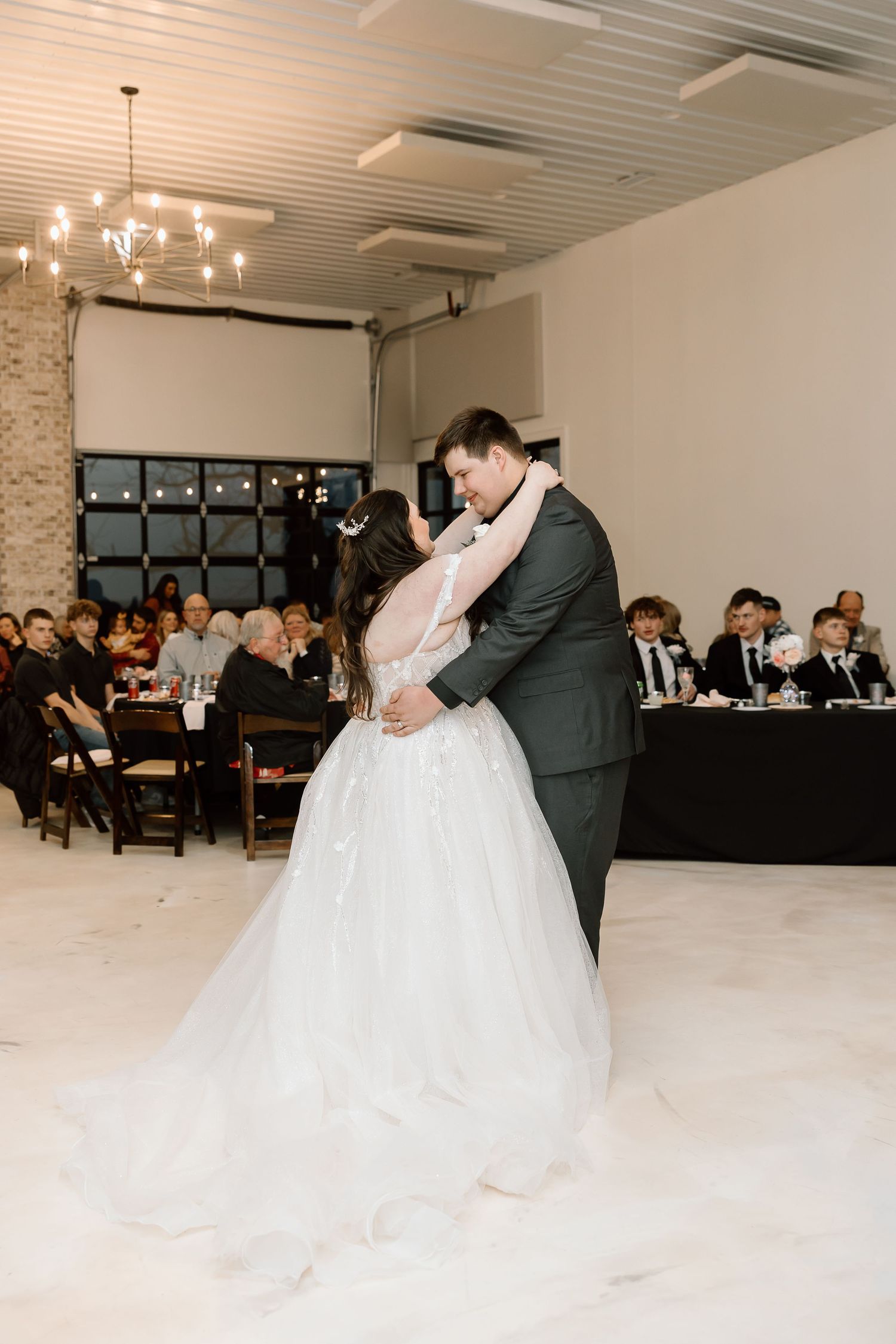 A bride and groom perform a romantic dip during their first dance at an indoor wedding reception.