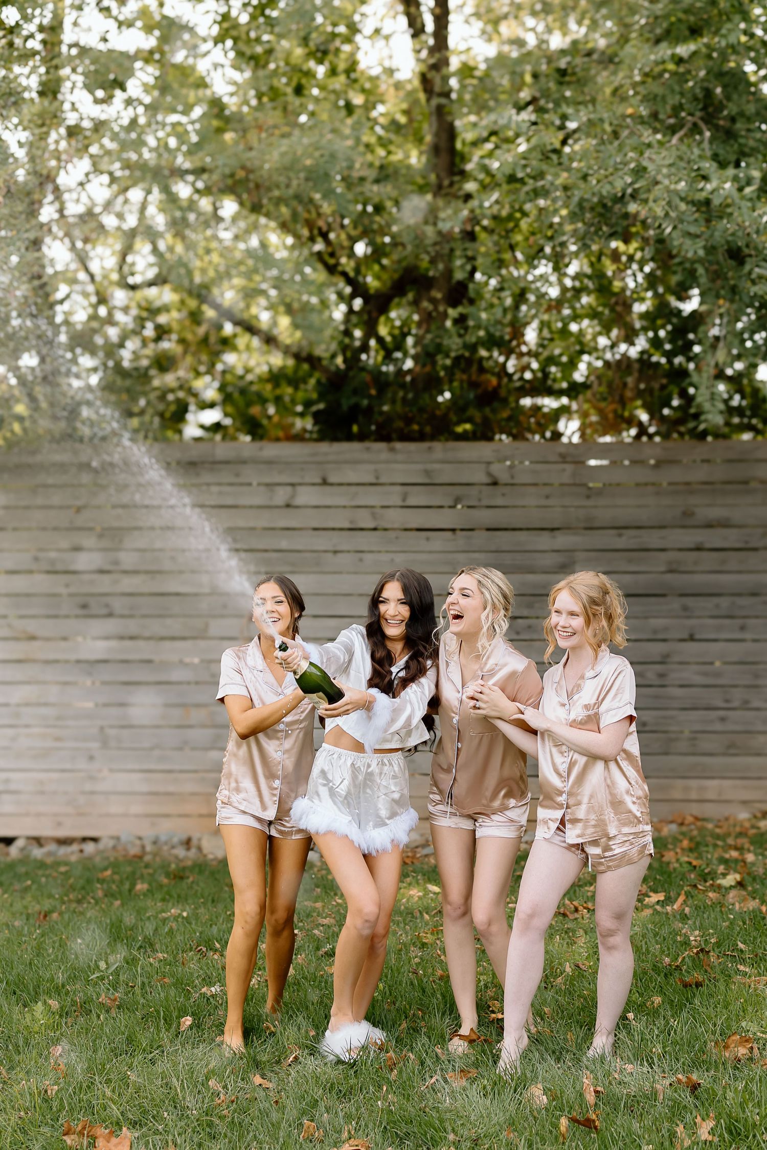 A group in matching neutral-toned outfits sits together on wooden benches in a backyard garden setting.