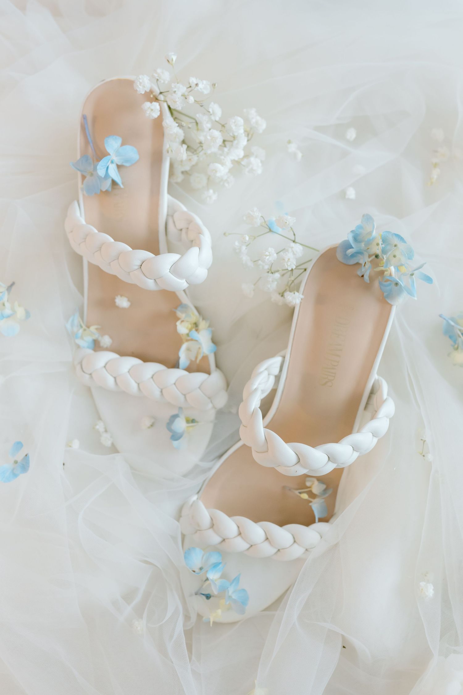 Elegant bridal heels with braided white straps adorned with delicate blue and white flowers on soft tulle fabric.