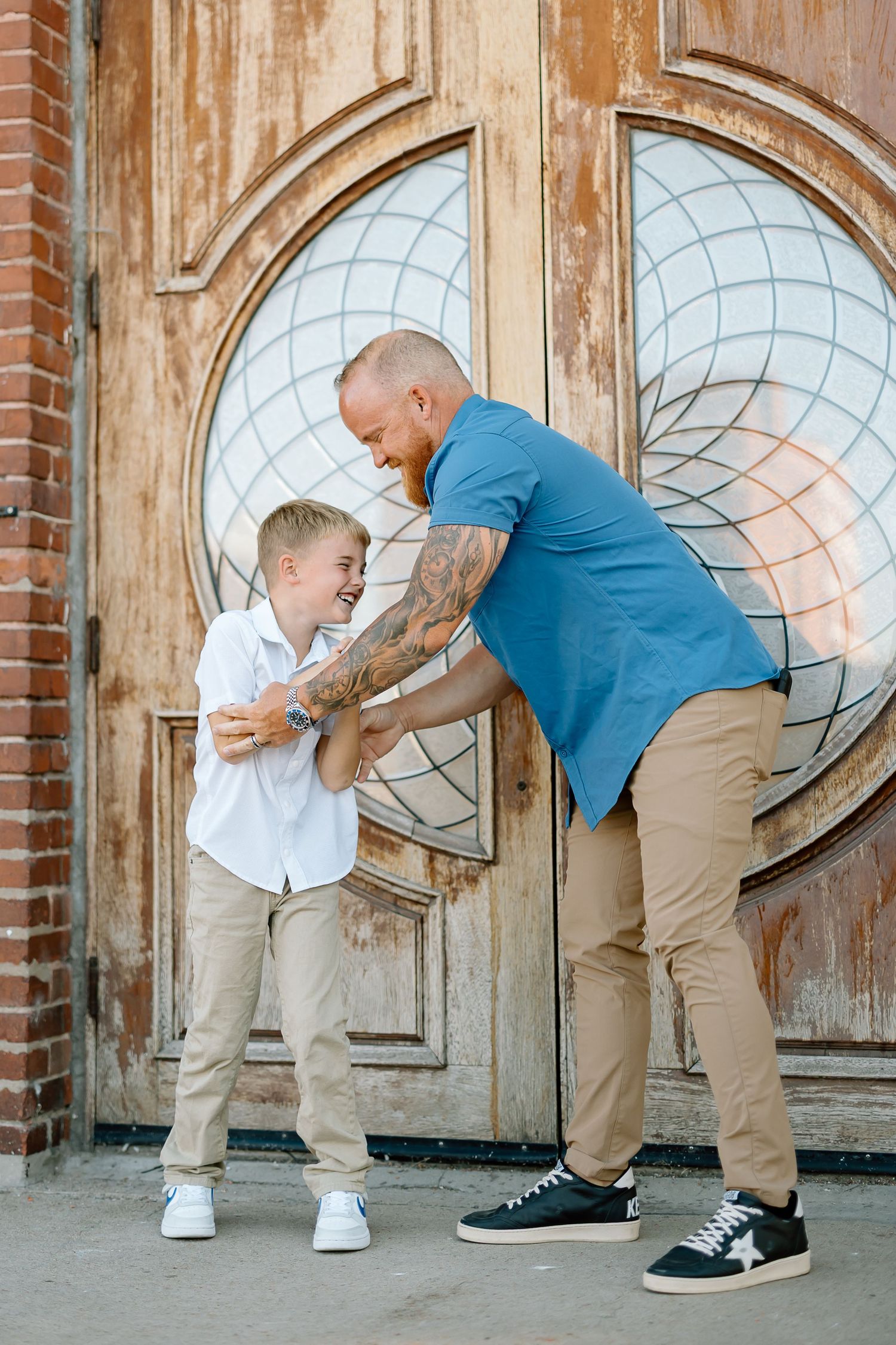 Two people share a playful moment in front of a vintage wooden door with decorative circular glass panels.