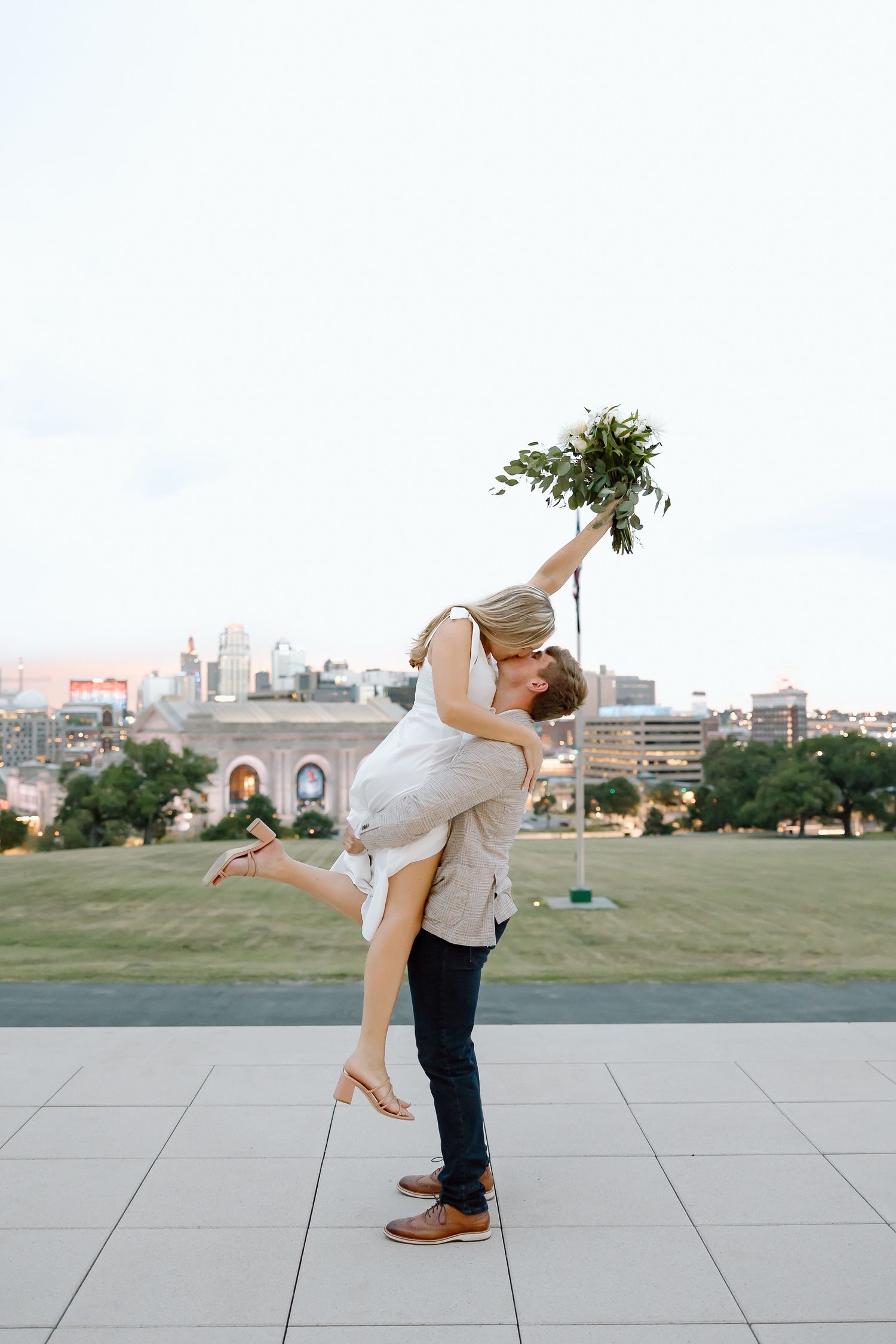 A couple performs a romantic dance lift sequence on a concrete plaza with a city skyline in the background.