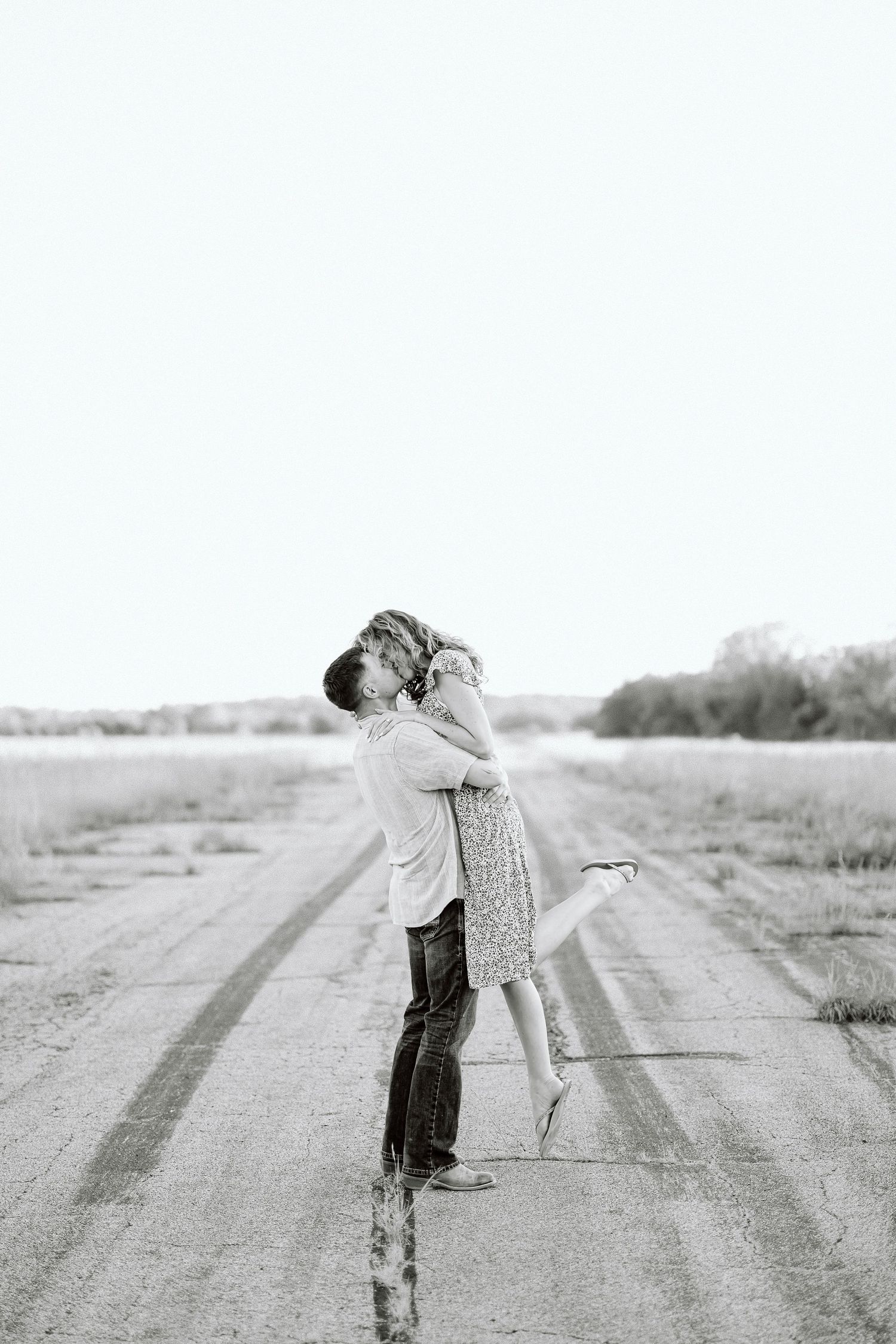 A romantic black and white photo shows a couple embracing on a rural dirt road.