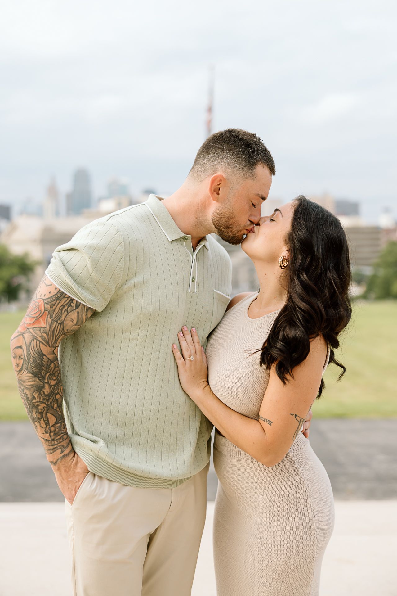 A couple in coordinated beige outfits sharing romantic moments against a city skyline backdrop.