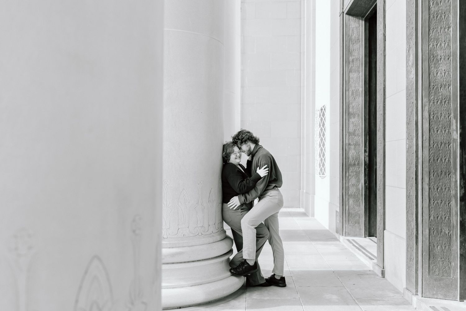 Black and white intimate portrait of a couple in tender embrace by a window.