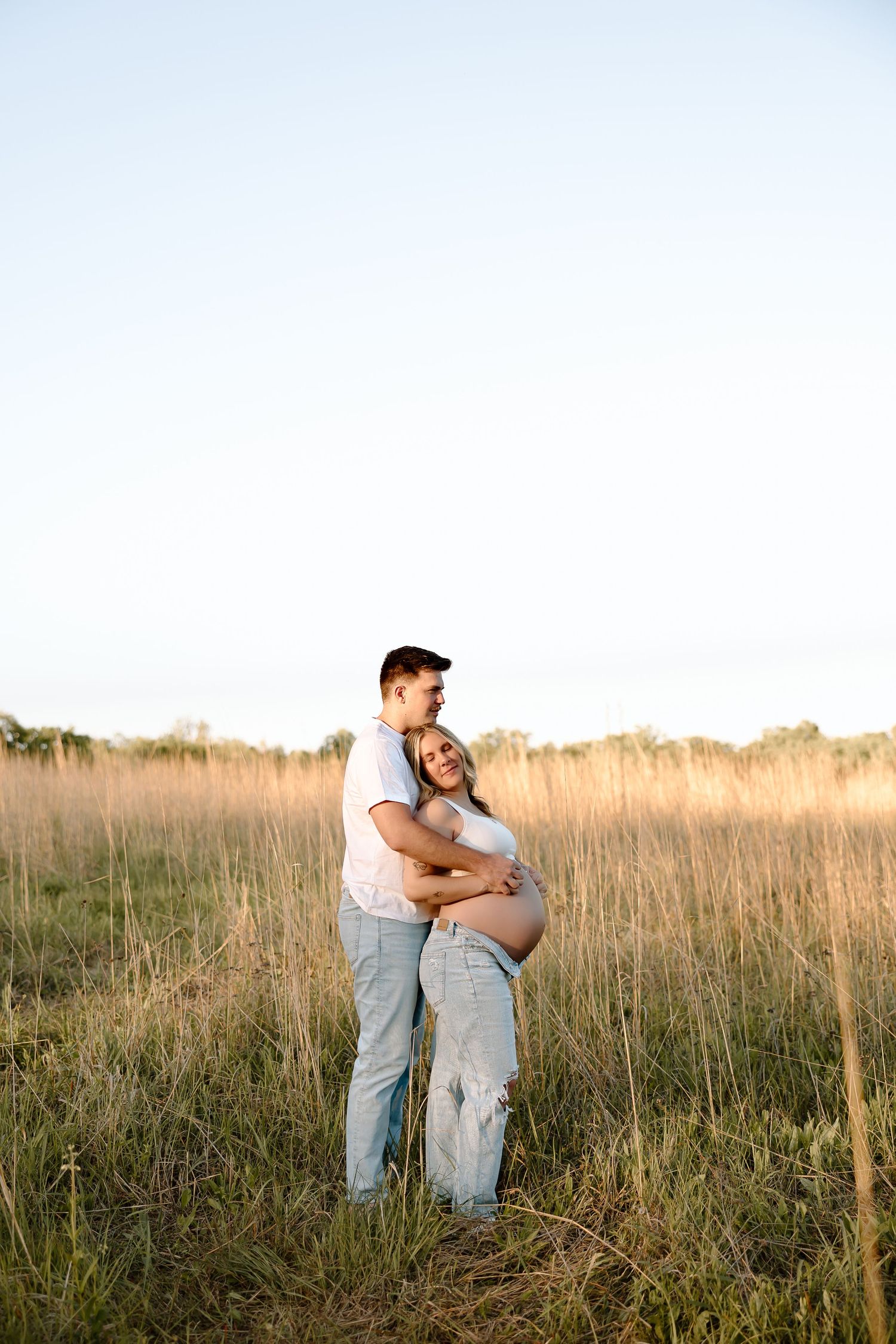 A couple embraces in a golden field of tall grass during sunset creating a romantic silhouette.