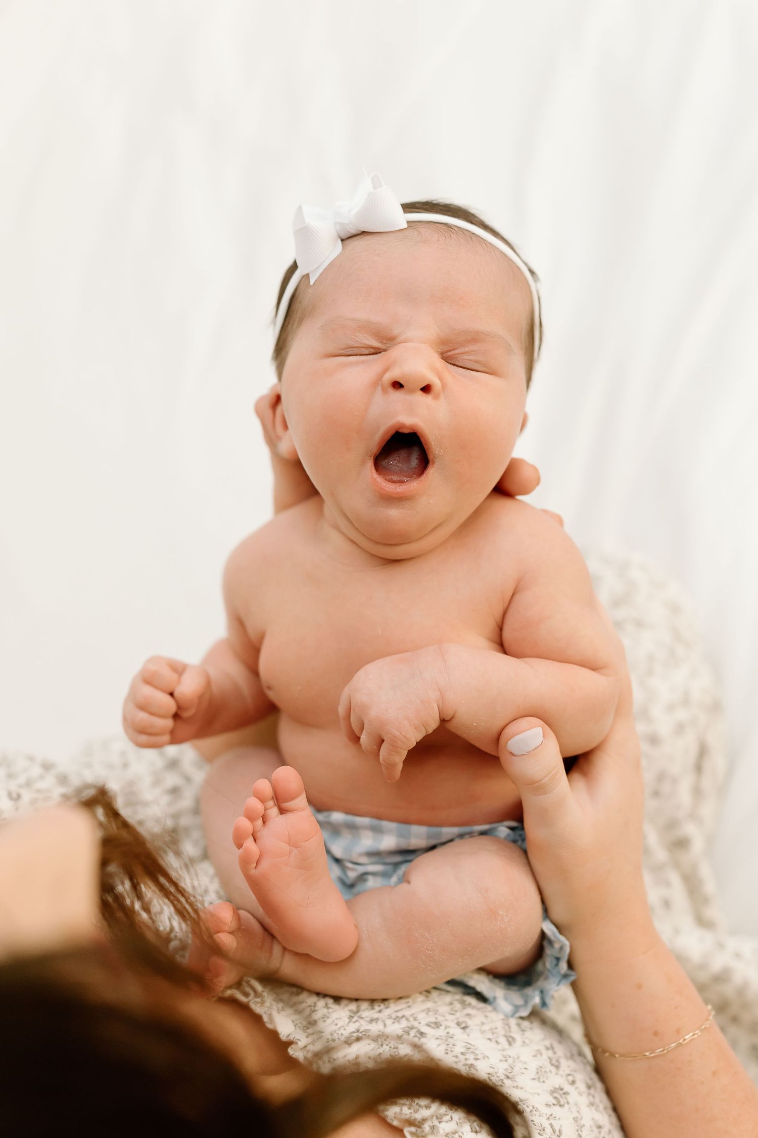 A newborn baby yawning while lying on soft white lace fabric during a professional photoshoot.