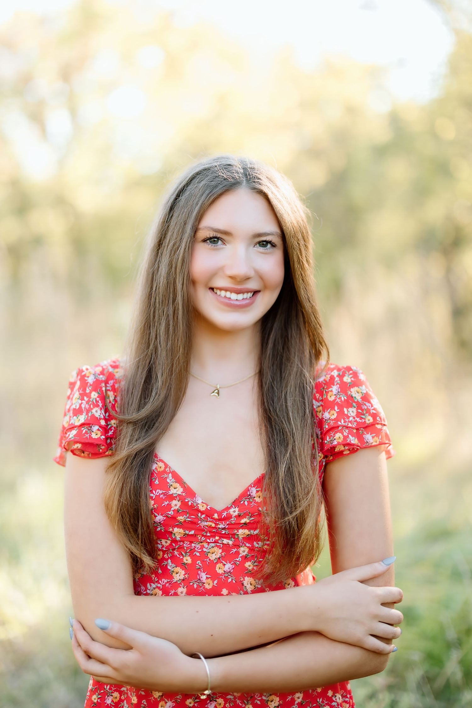 A person in a red floral dress poses outdoors against a soft natural background.