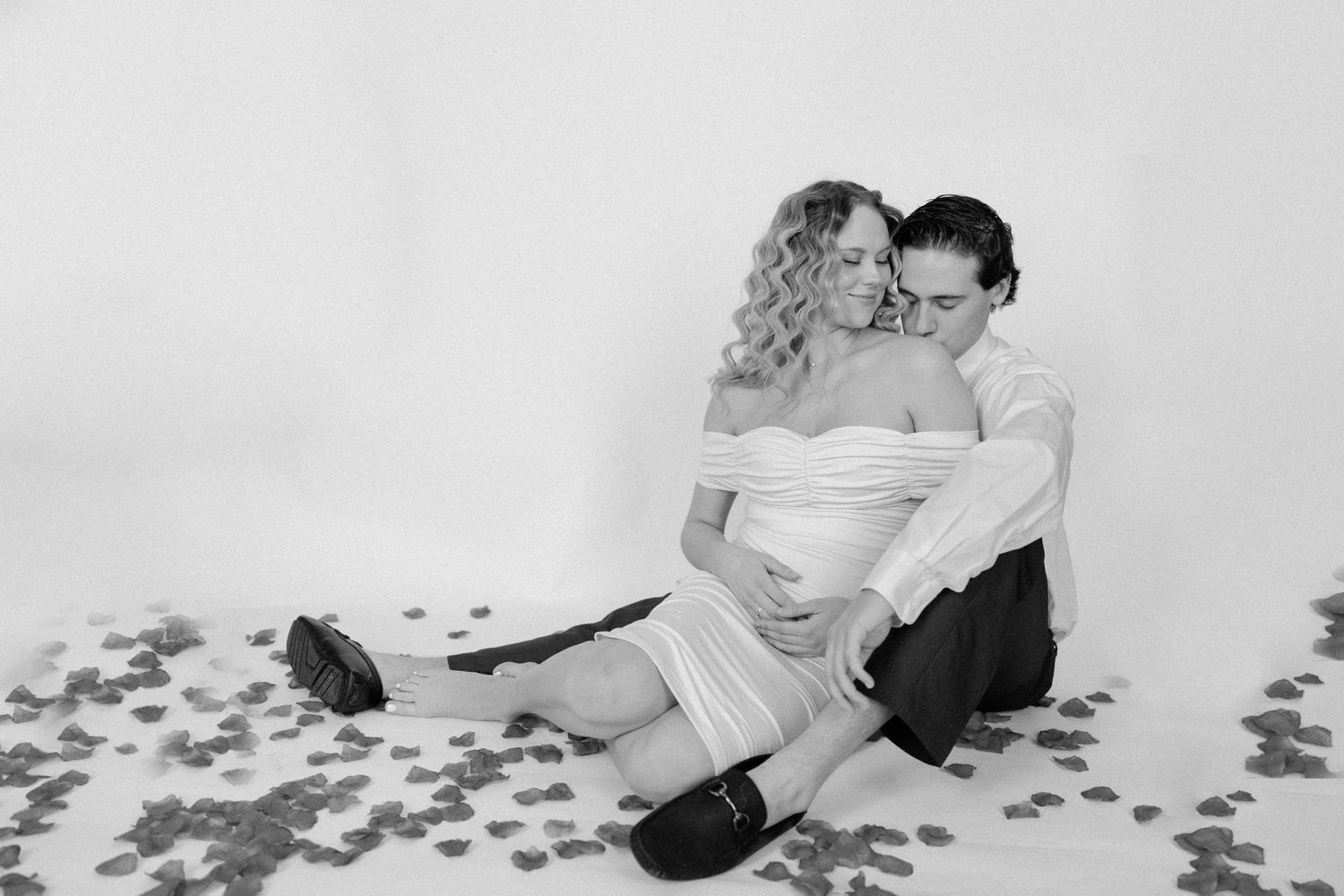 A romantic black and white photo of a couple sitting together surrounded by scattered rose petals.