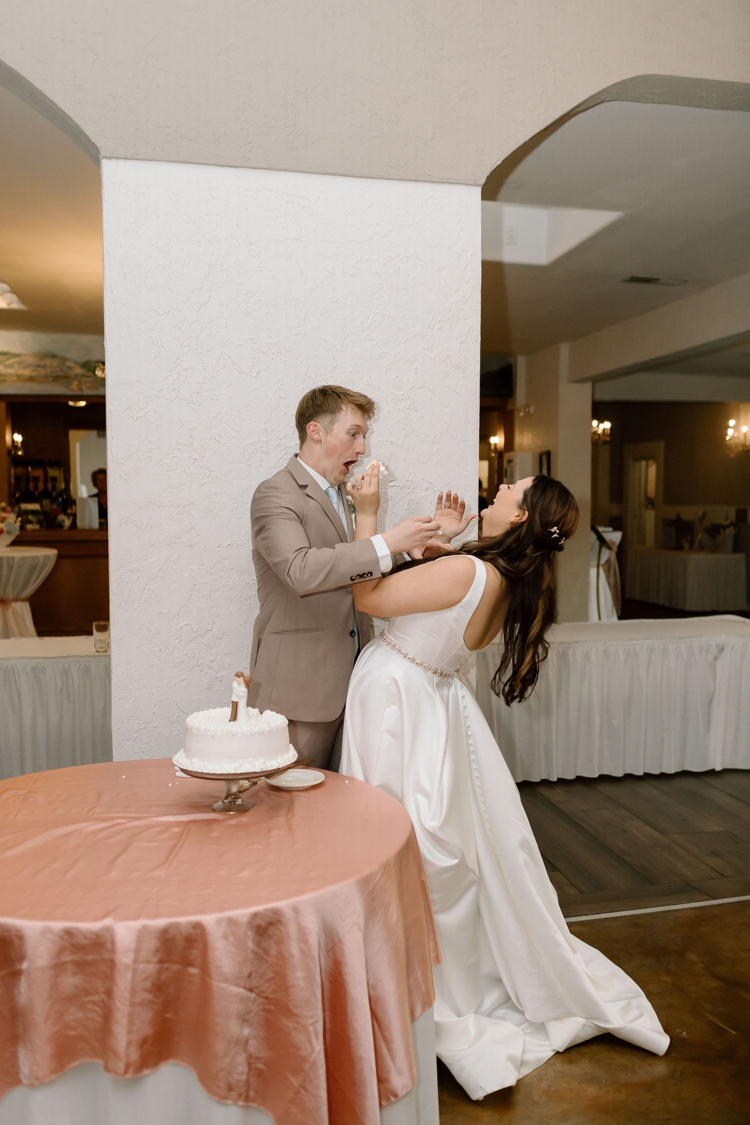 Playful moment between newlyweds as they share cake during their wedding reception with peach tablecloth decor.
