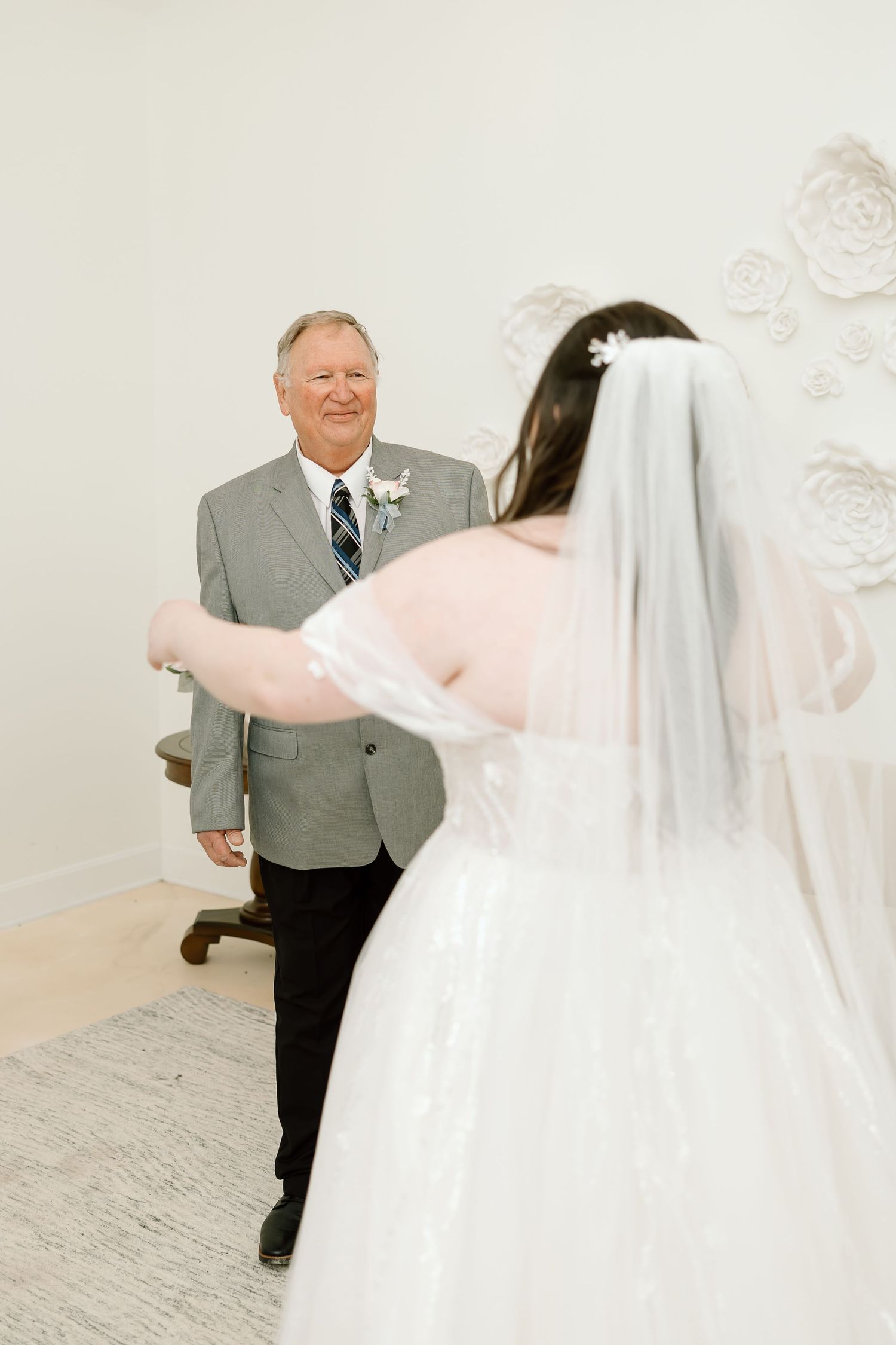 A heartwarming first look moment between a bride in white dress and someone in a gray suit at a wedding venue.