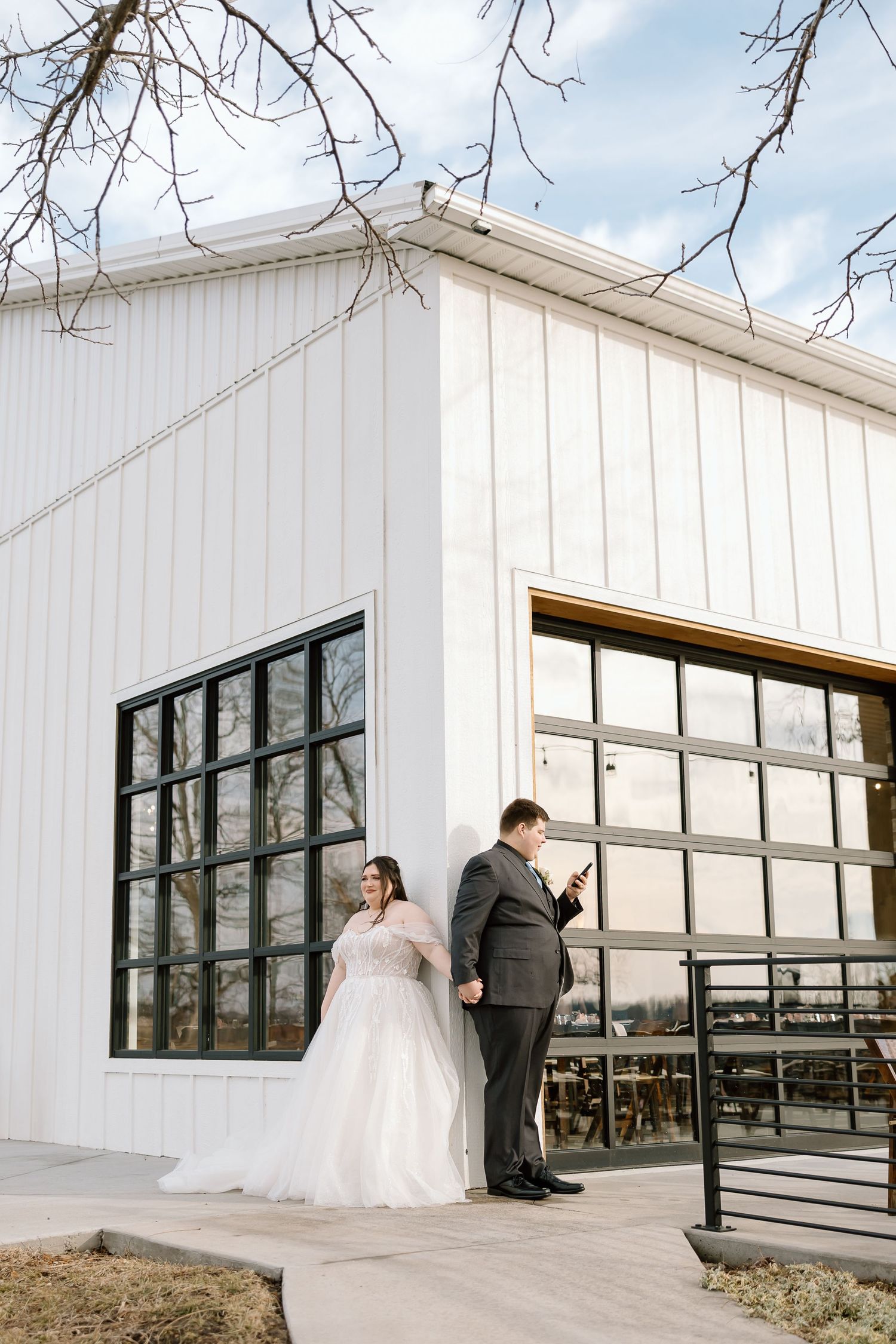 A couple stands on a deck outside a modern white building with large windows during their wedding.