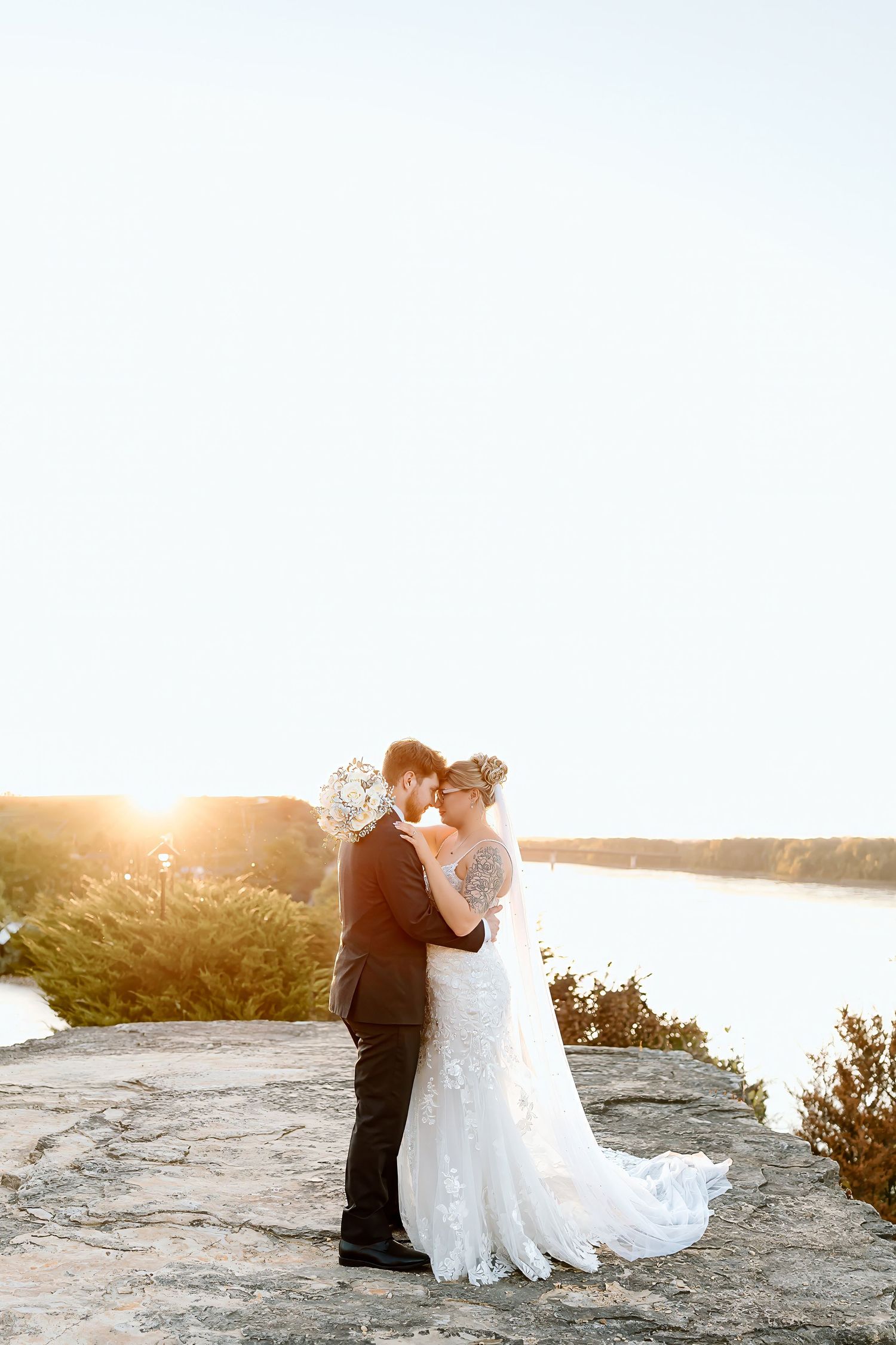 A romantic sunset silhouette of a couple on a rocky cliff overlooking a serene lake.