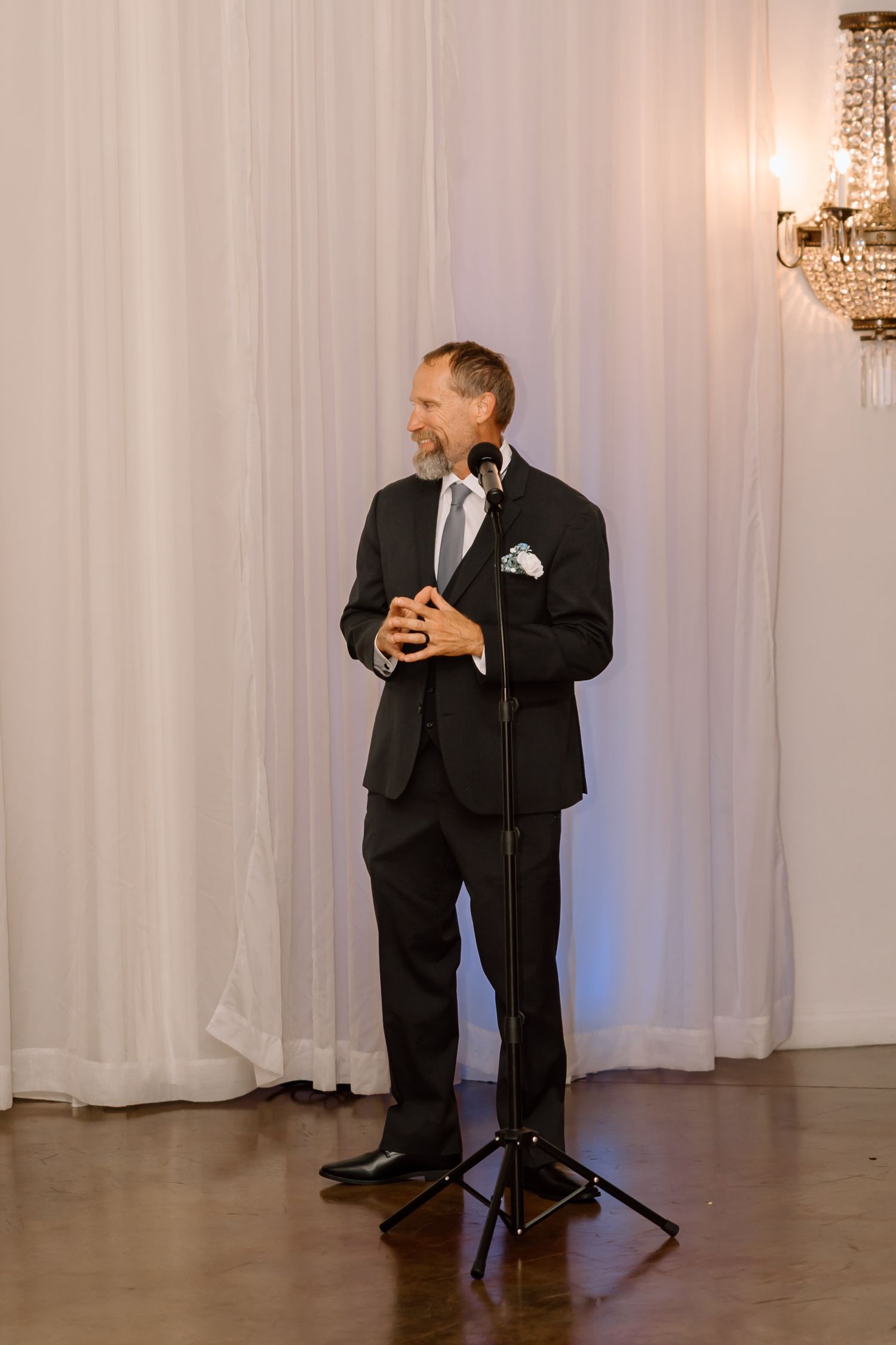 A couple performs an elegant dance move in a white-draped reception hall with chandeliers.
