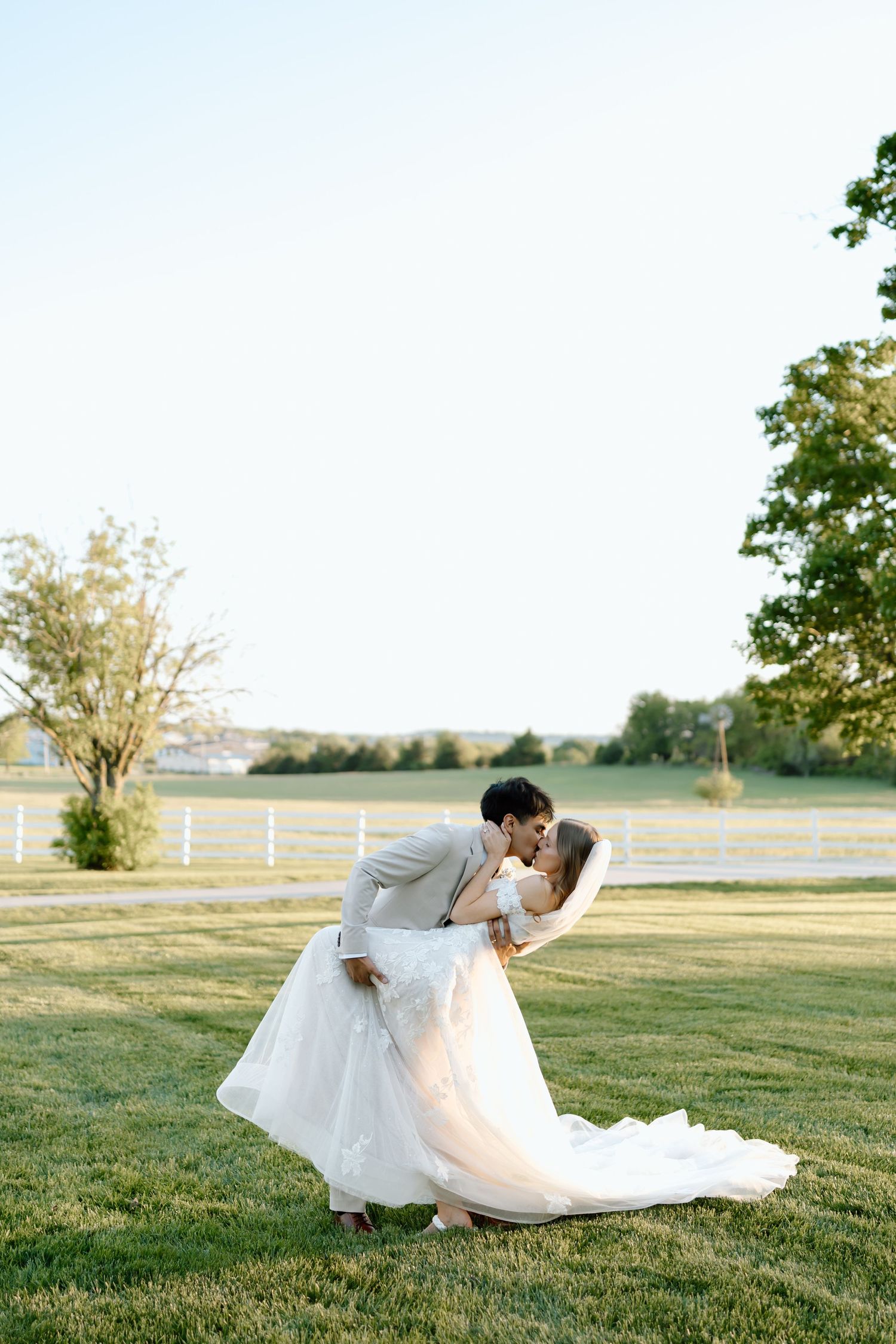 A groom dips his bride for a romantic kiss on a lush green lawn during their outdoor wedding ceremony.