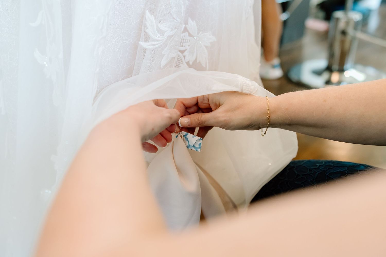 Close-up of hands fastening a delicate blue wedding garter on a bride in a lace bridal gown.