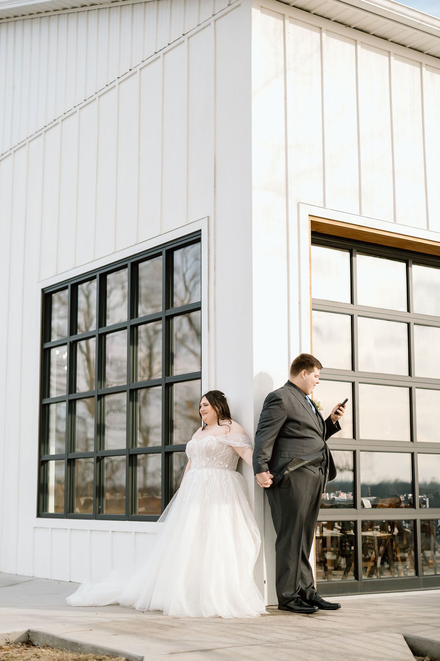Couple taking creative wedding photos outside modern white building with large windows.