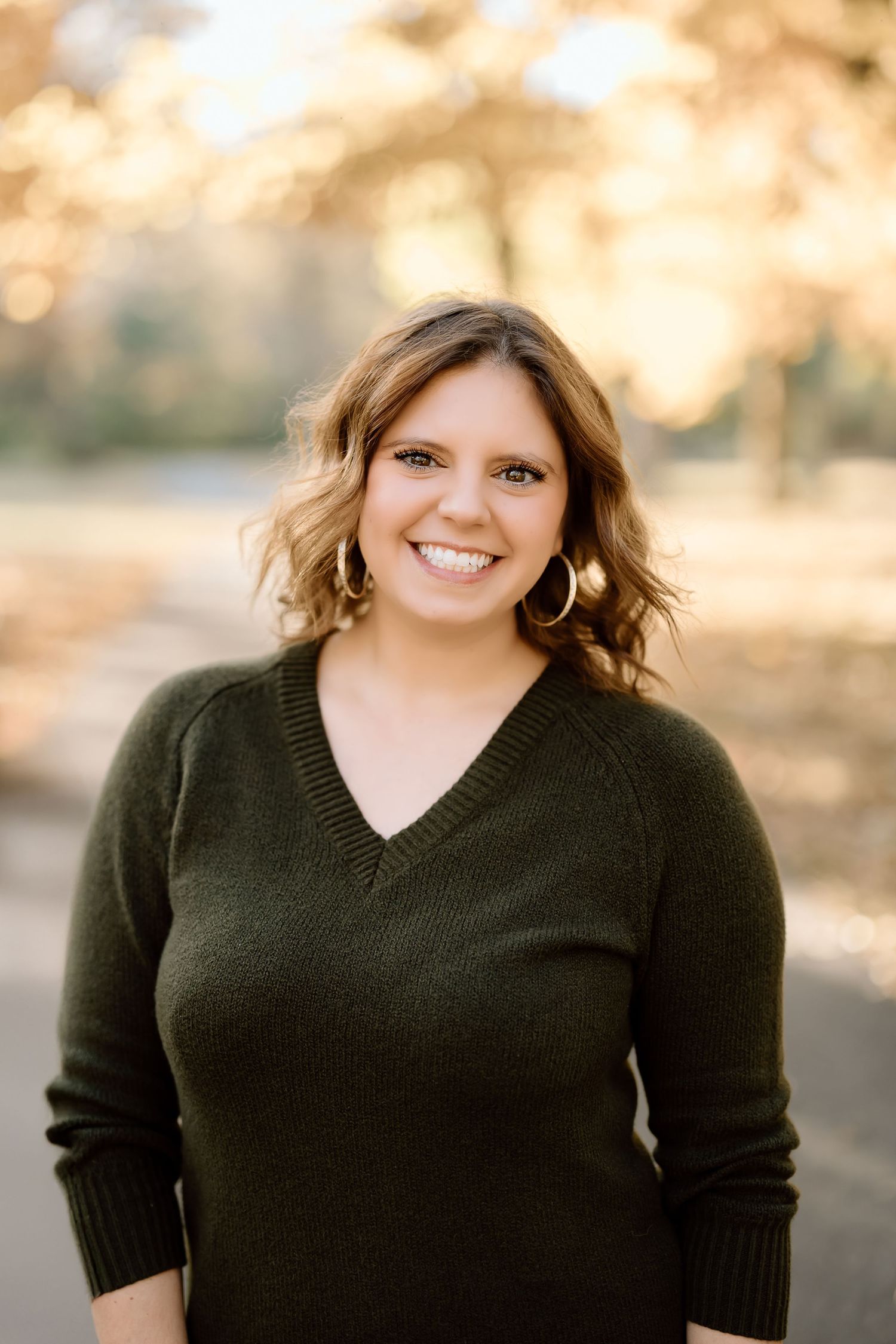Portrait of a woman in a dark green sweater standing outdoors in autumn.