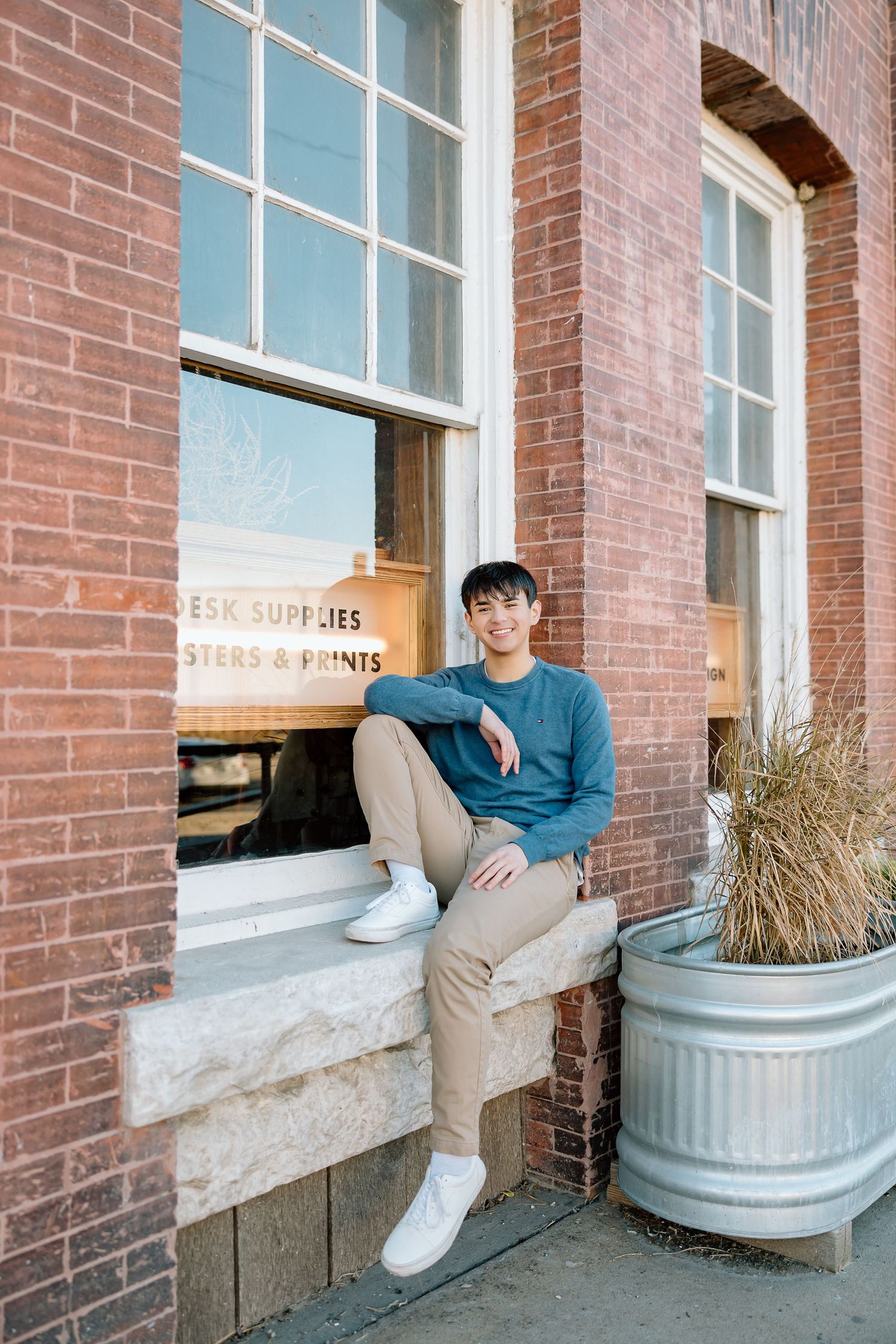 Casual pose on stone windowsill wearing blue sweater and khakis.