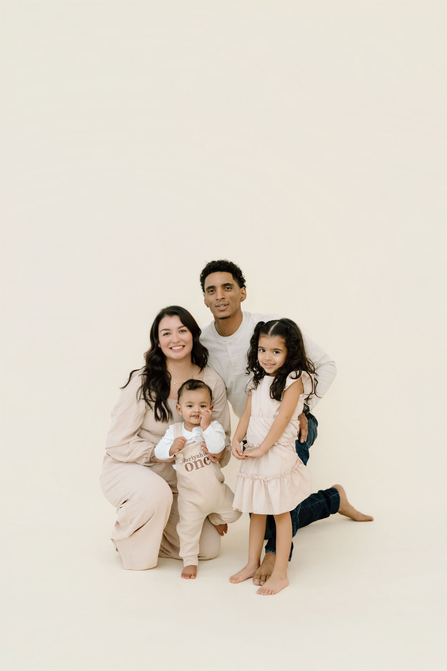 A family in light colored clothing sits together on a white background for a minimalist portrait session.