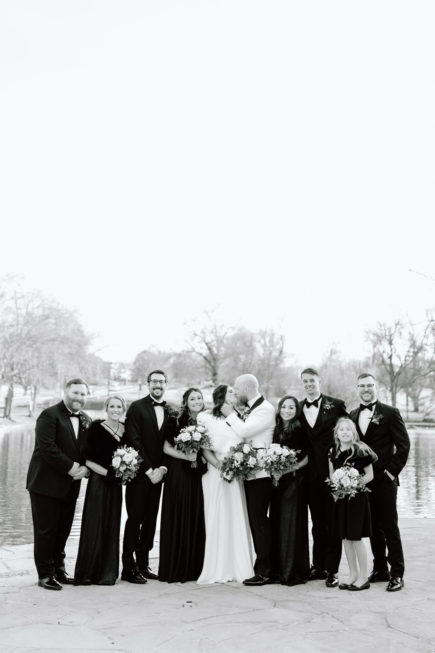 Wedding party in black and white formal attire poses together outdoors on a misty day.