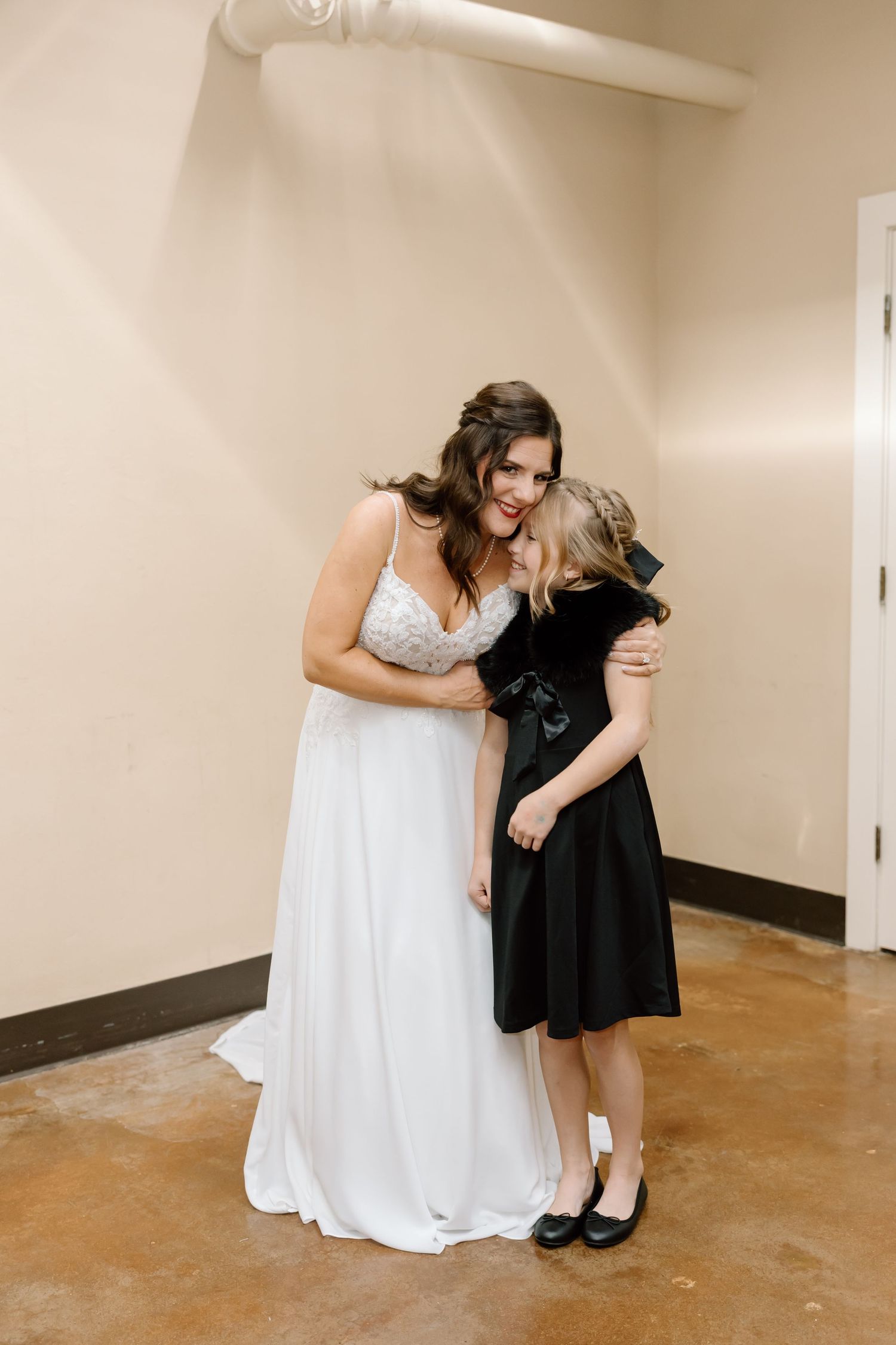 A person in a white wedding gown embraces someone wearing a black dress in an indoor setting.
