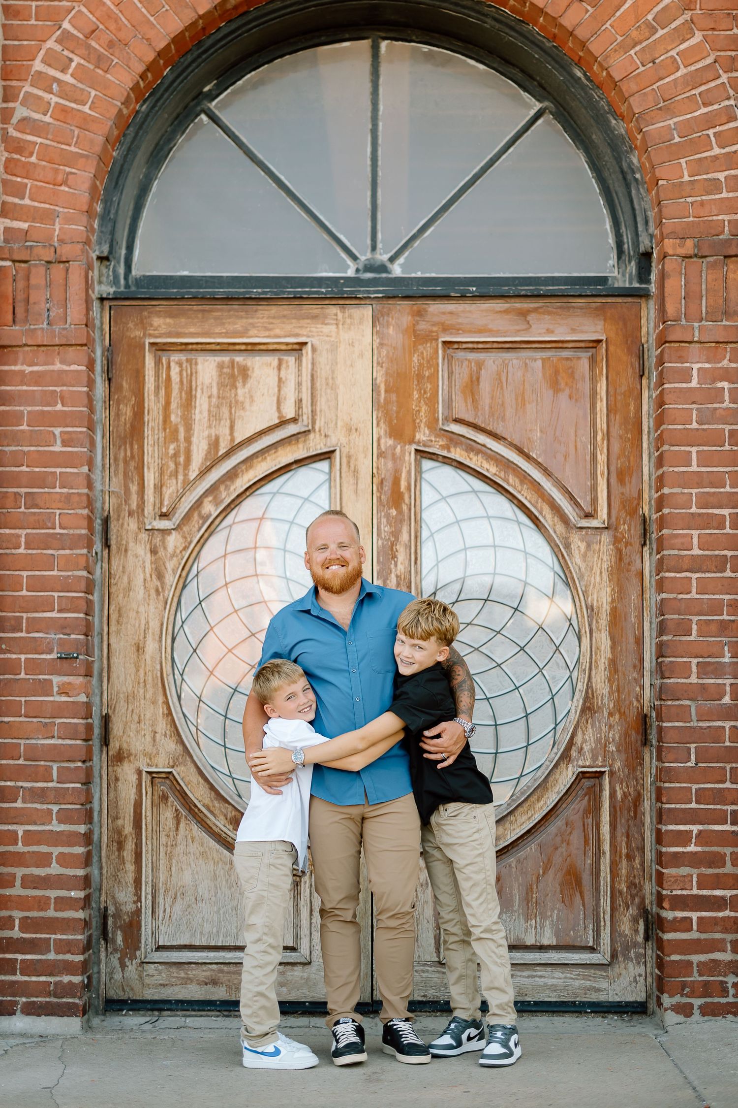 A group poses in front of an ornate wooden church door with arched windows and brick walls.