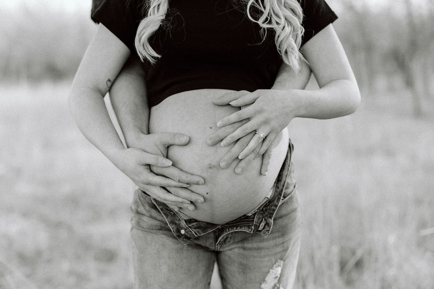 Black and white maternity photo series showing close-up shots of pregnant belly being cradled by hands in outdoor setting.