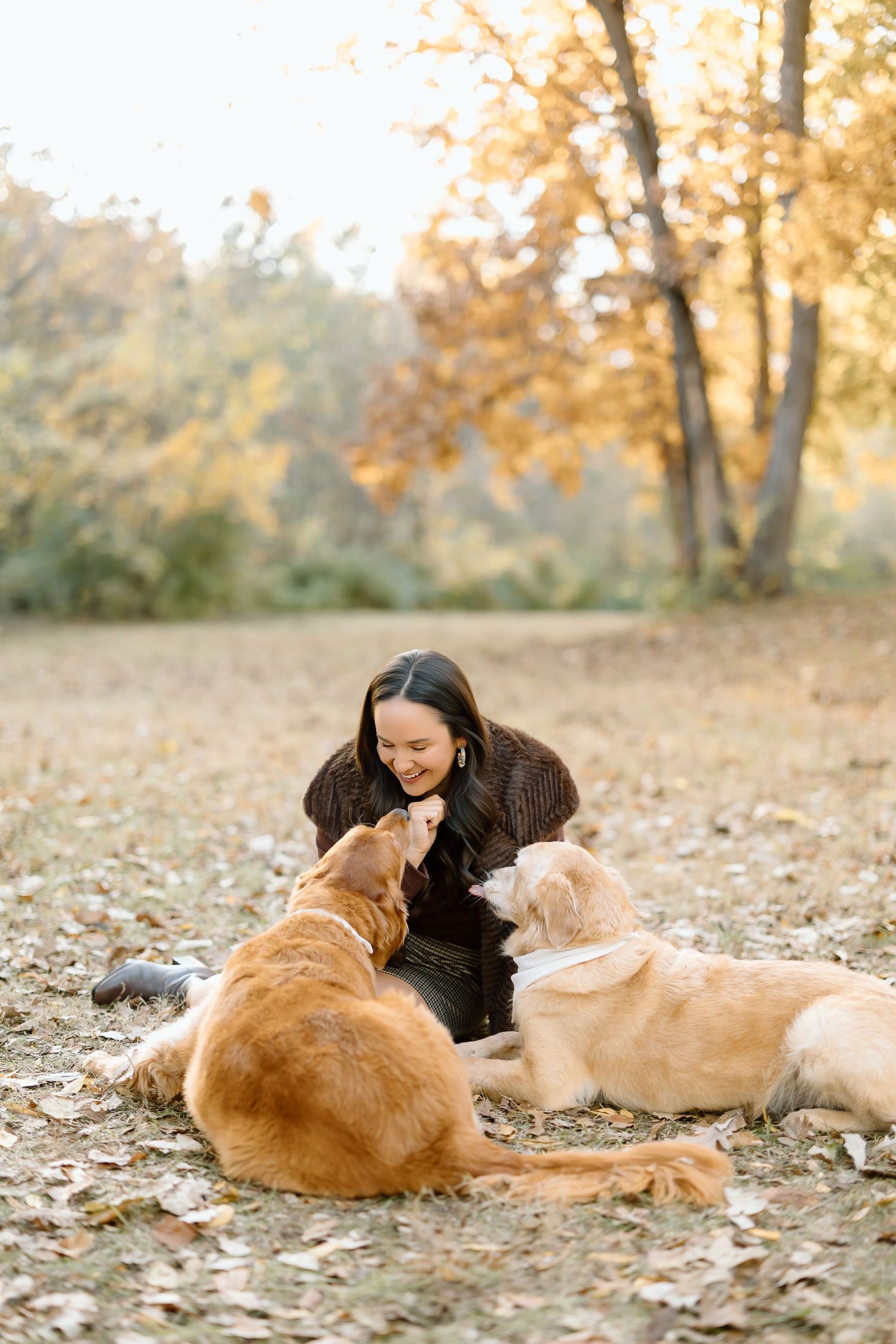 A person lies on autumn leaves cuddling with a golden retriever dog in a warm outdoor setting.