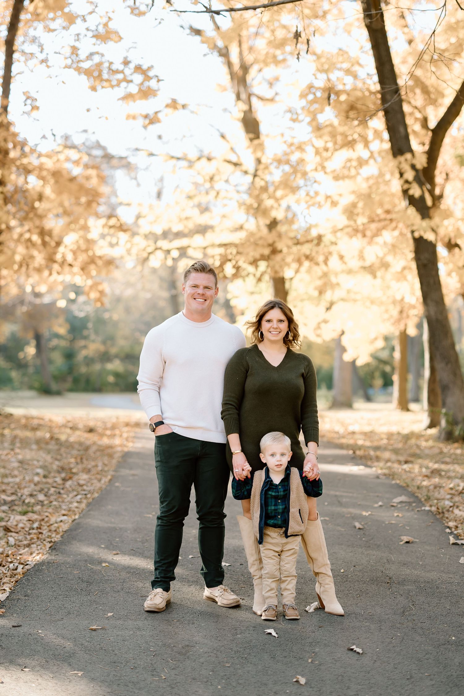 A family stands together on a paved path surrounded by golden autumn trees.