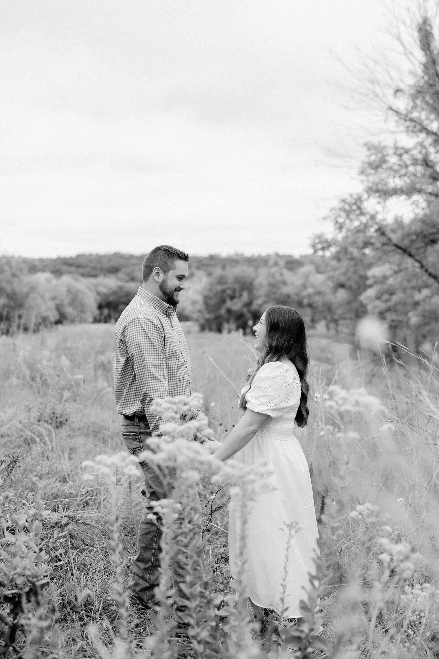 Black and white portrait of couple standing in dreamy meadow surrounded by wildflowers.
