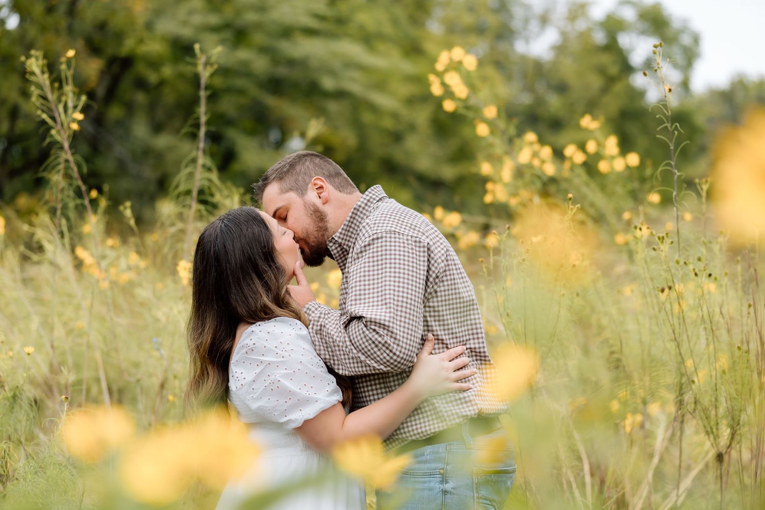 A couple shares an intimate kiss amid tall grasses and yellow wildflowers.