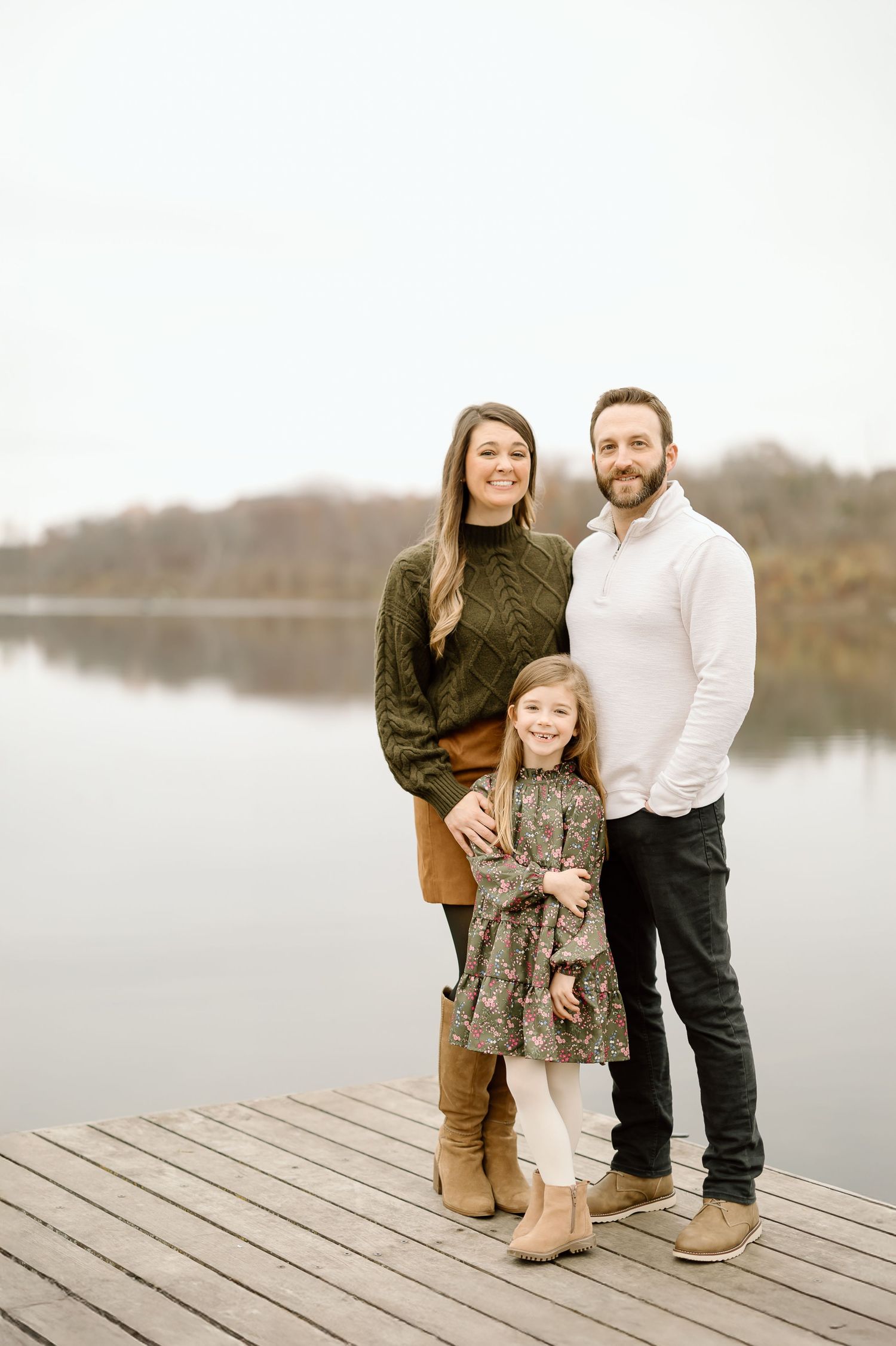 Family portrait on wooden dock with calm lake and fall foliage in background.