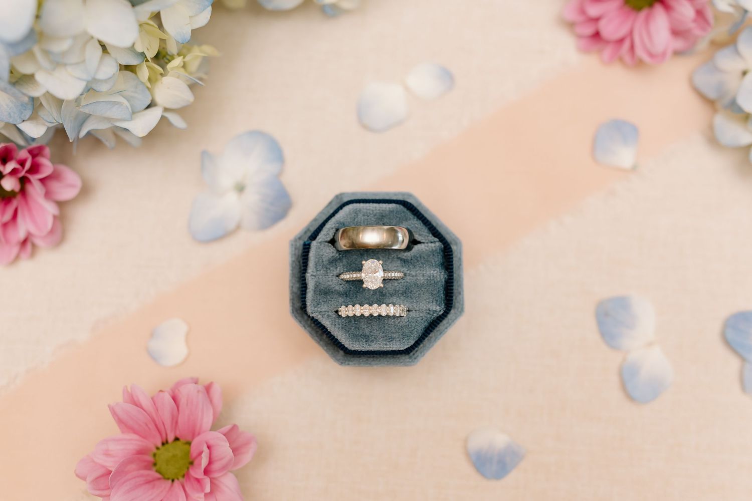 Wedding rings nestled in a navy blue box surrounded by delicate pink and white flowers.