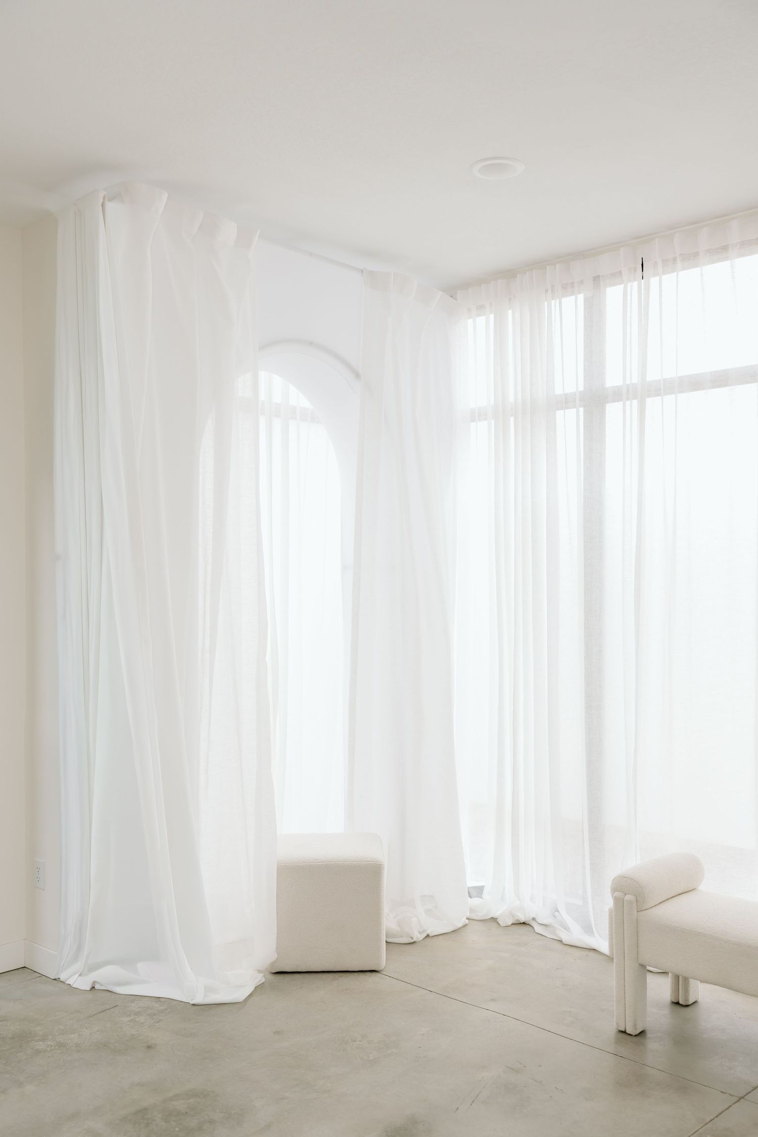 A minimalist white room with sheer curtains and concrete floors creating a bright, ethereal atmosphere.