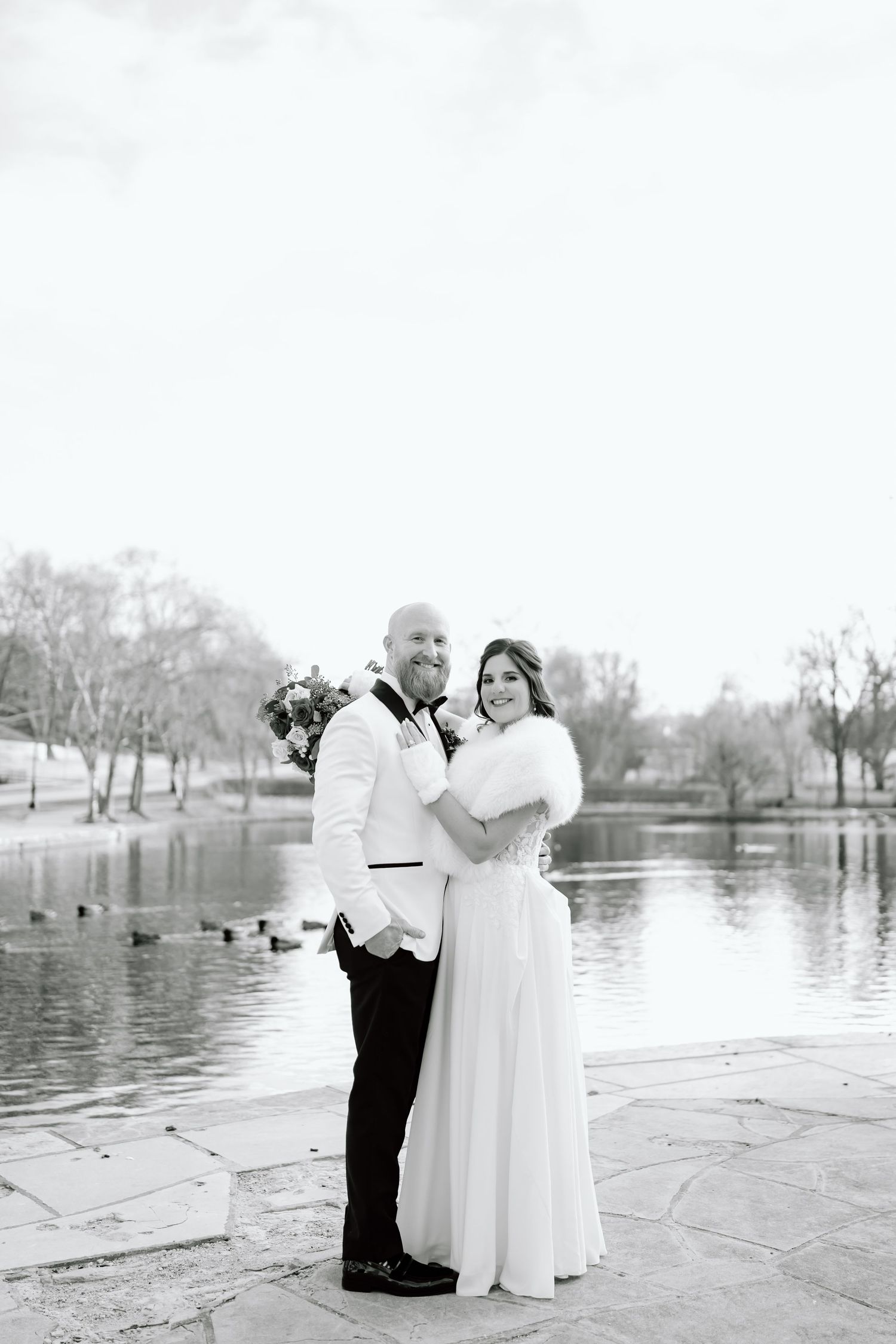 A romantic wedding couple shares intimate moments by a serene lake in black and white photography.